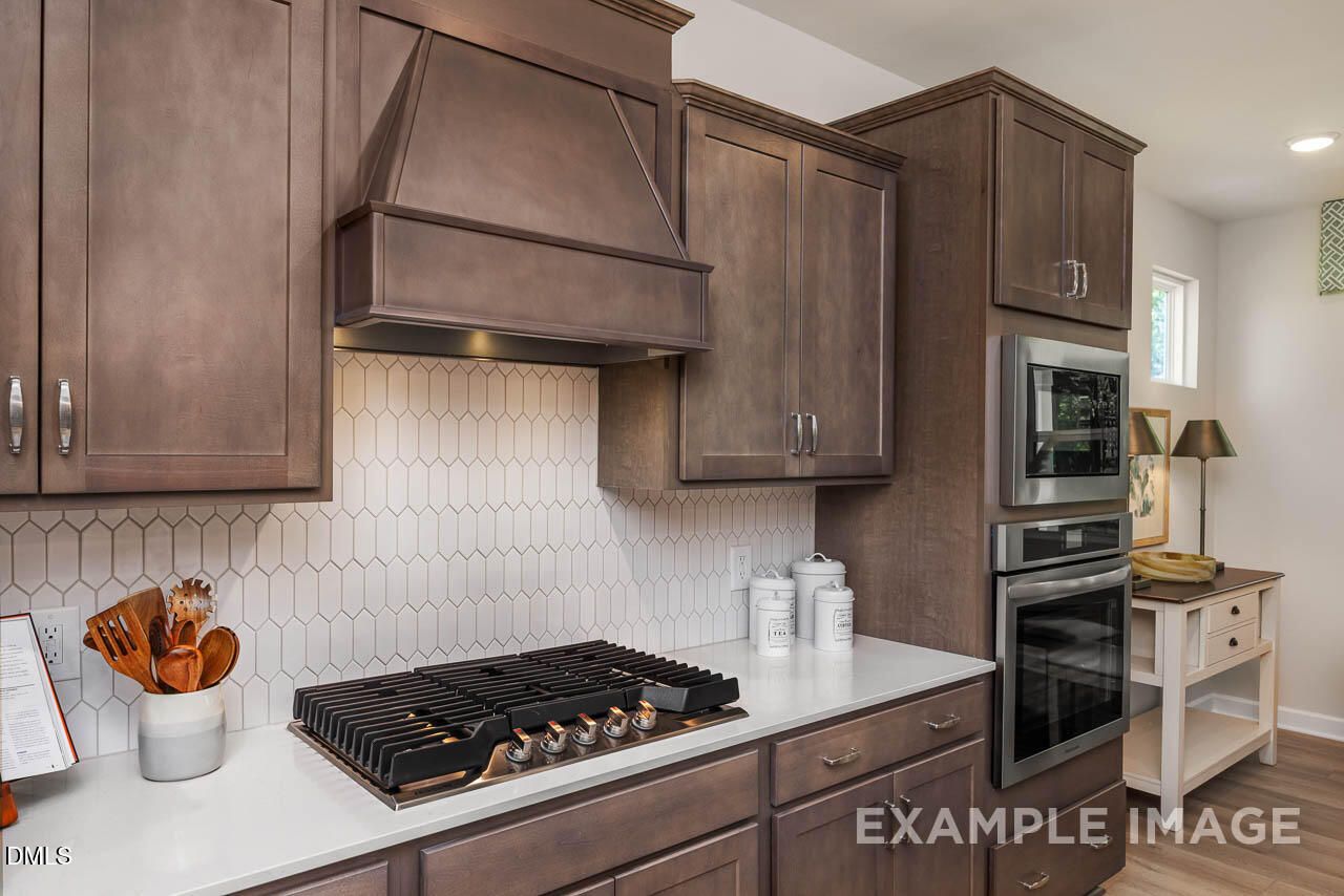 Elegant kitchen with taupe shaker cabinets, hexagonal subway backsplash, quartz counters, gas range, and stainless appliances in Davidson Homes The Willow B, Wake Forest