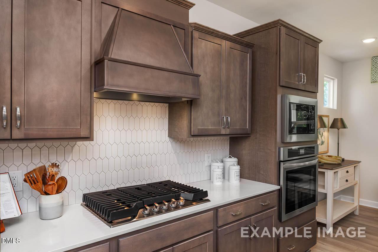Elegant kitchen with taupe shaker cabinets, hexagonal subway backsplash, quartz counters, gas range, and stainless appliances in Davidson Homes The Willow B, Wake Forest