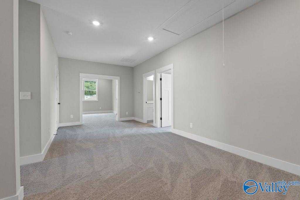 Spacious hallway with neutral gray walls, plush carpet floors, and white doors in 5-bedroom Oxford plan home, Owens Cross Roads, Alabama