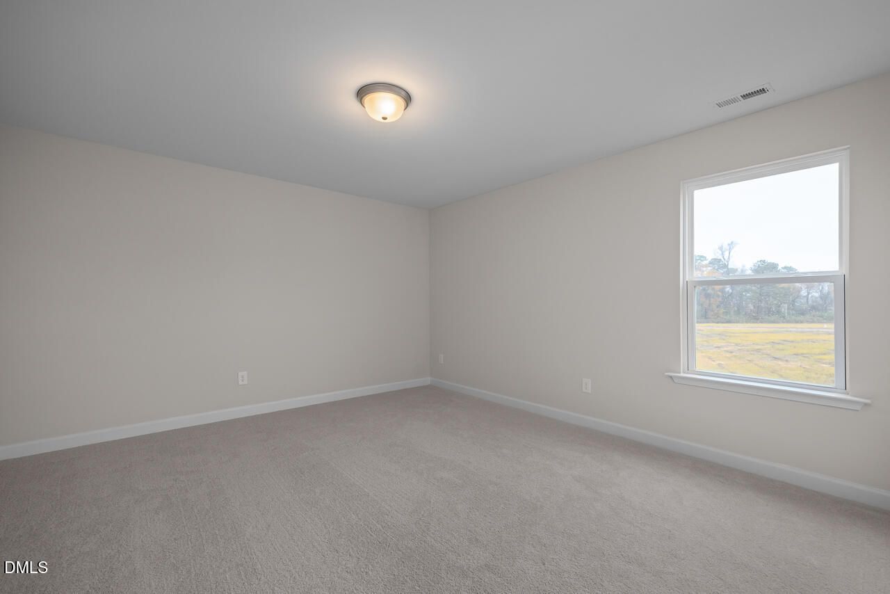 Spacious empty bedroom with light gray walls, neutral carpet, ceiling light, and window overlooking rural fields in Davidson Homes The Cypress D II, Angier, NC