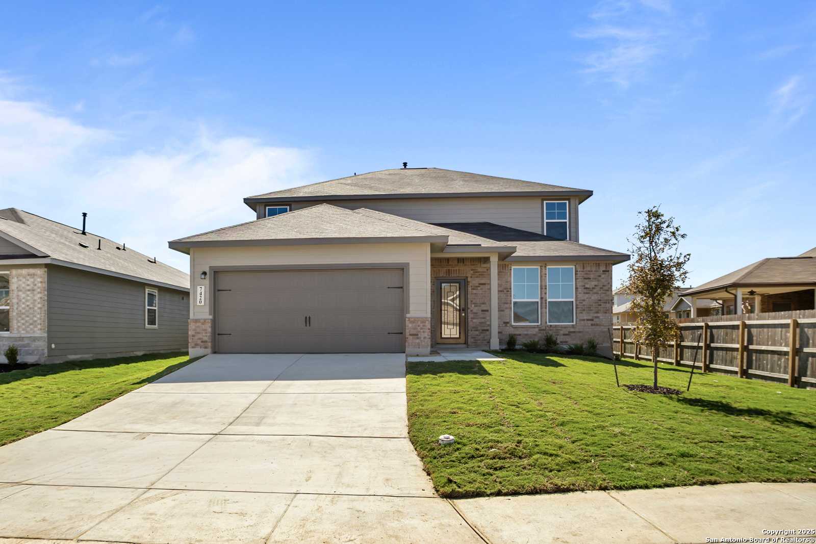 Modern two-story 4-bedroom home with beige siding, brick accents, 2-car garage, driveway, and lush front yard in Horizon Pointe, Converse, Texas
