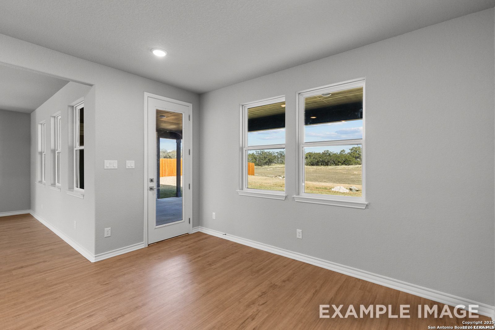 Bright living area with wood-style flooring, large windows, and patio access in Davidson Homes Oxford F, Potranco Oaks.