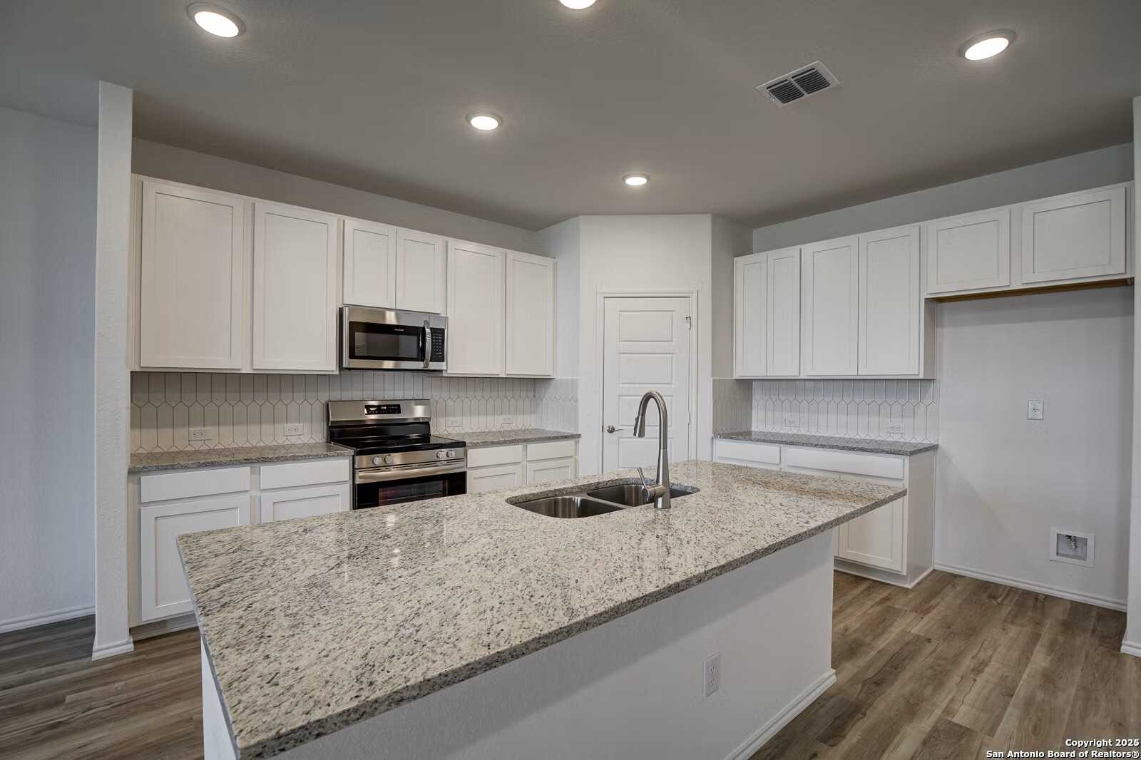 Modern white kitchen with granite island, stainless steel appliances, subway tile backsplash in Davidson Homes The Douglas B, Seguin, TX