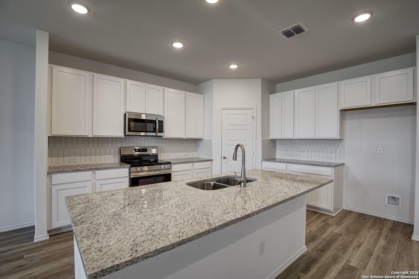 Modern white kitchen with granite island, stainless steel appliances, subway tile backsplash in Davidson Homes The Douglas B, Seguin, TX