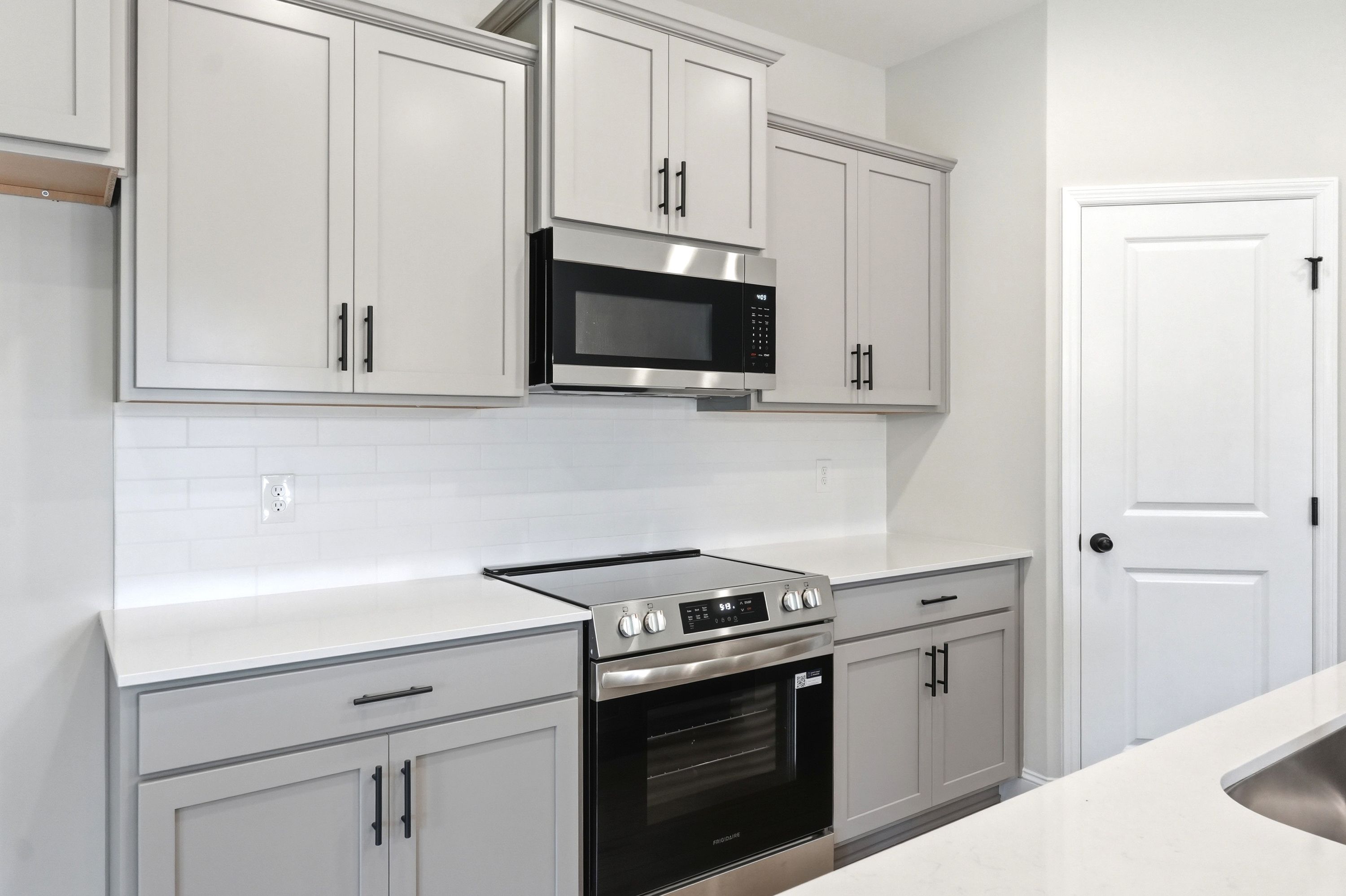 Modern kitchen in The Russell A featuring gray shaker cabinets, stainless steel appliances, and white quartz countertops.