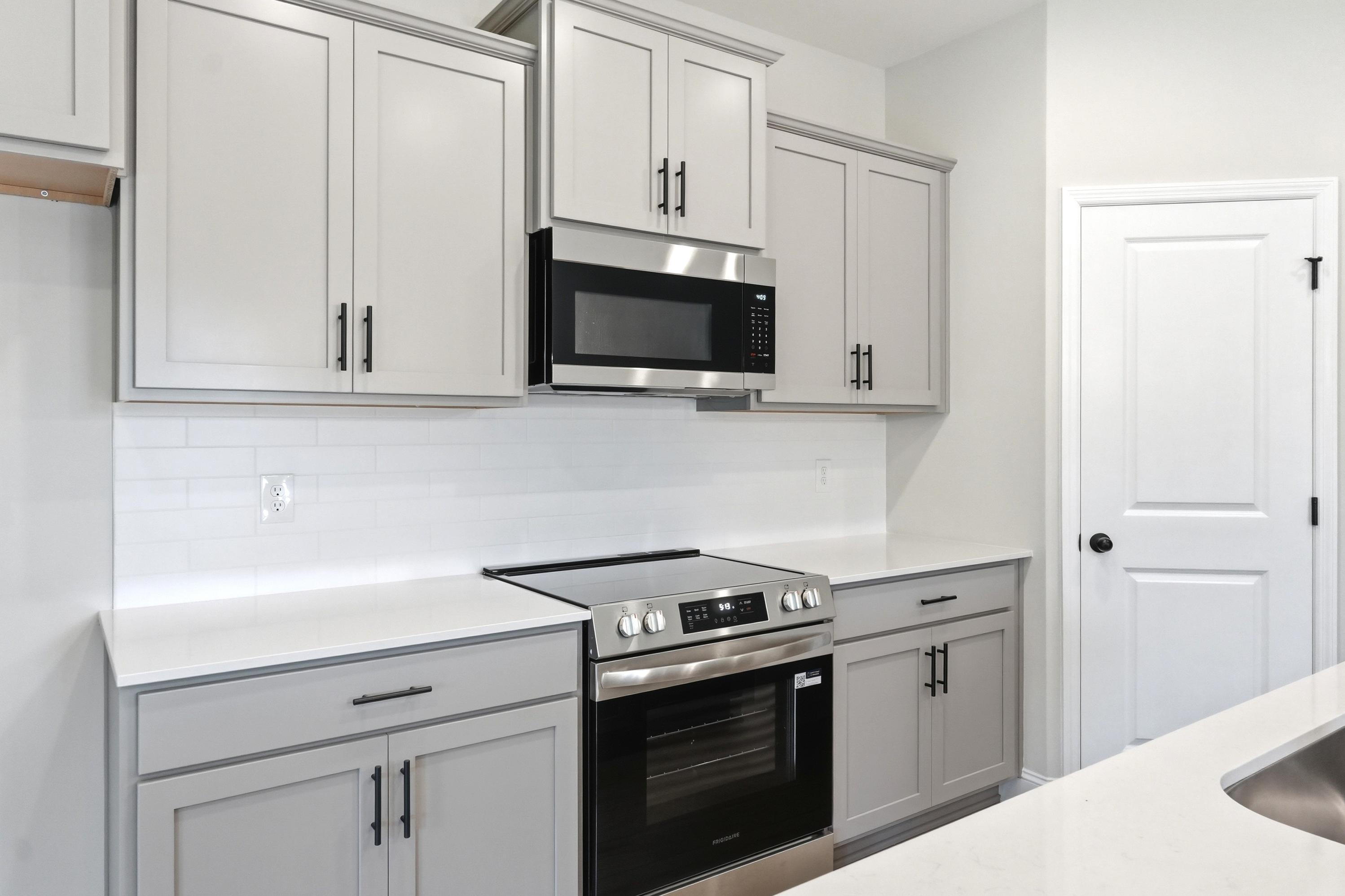 Modern kitchen in The Russell A featuring gray shaker cabinets, stainless steel appliances, and white quartz countertops.