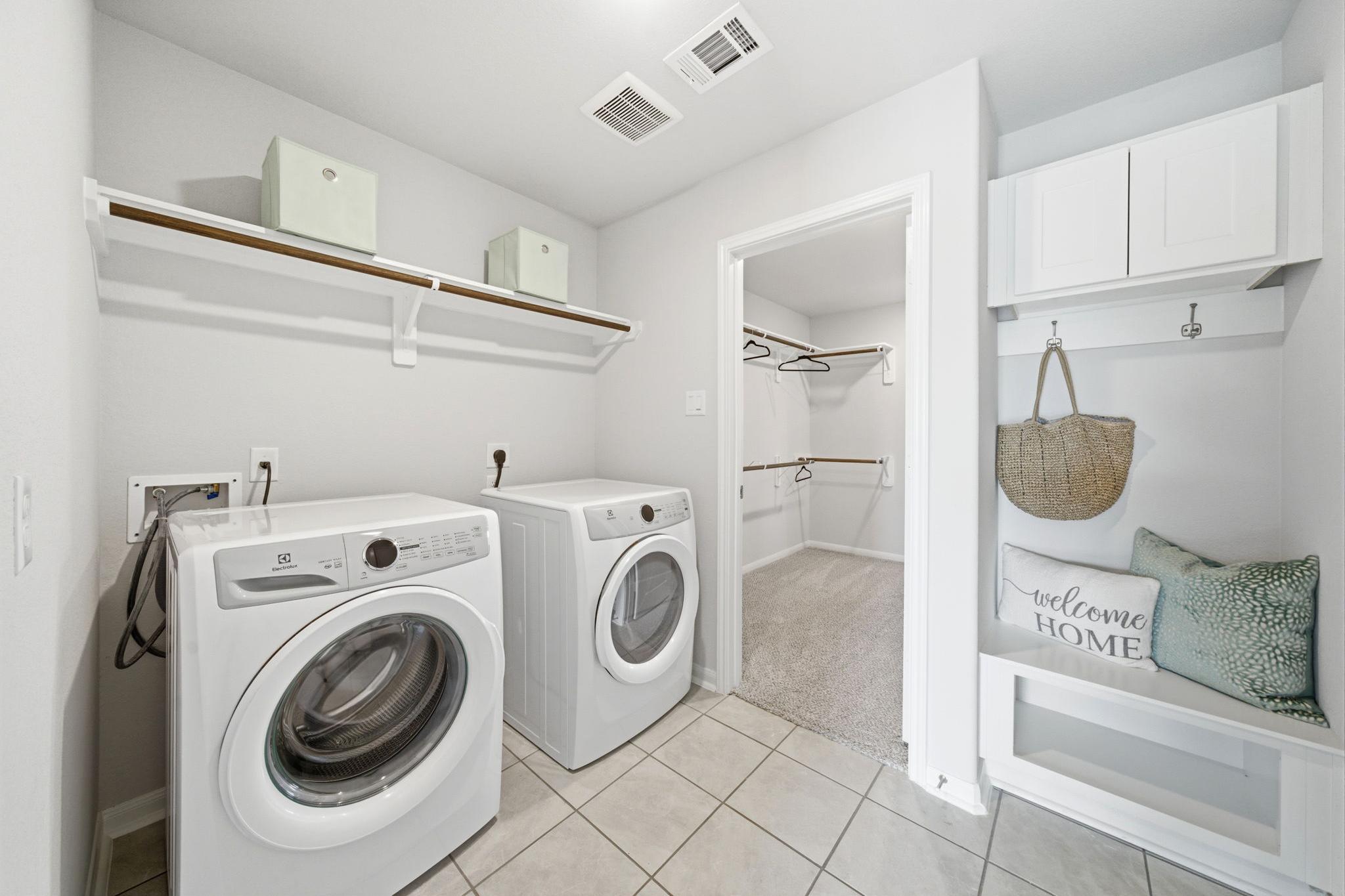 Spacious laundry room at Sunterra in Katy Texas by Davidson Homes with white washer dryer cabinets shelves and welcome home bench