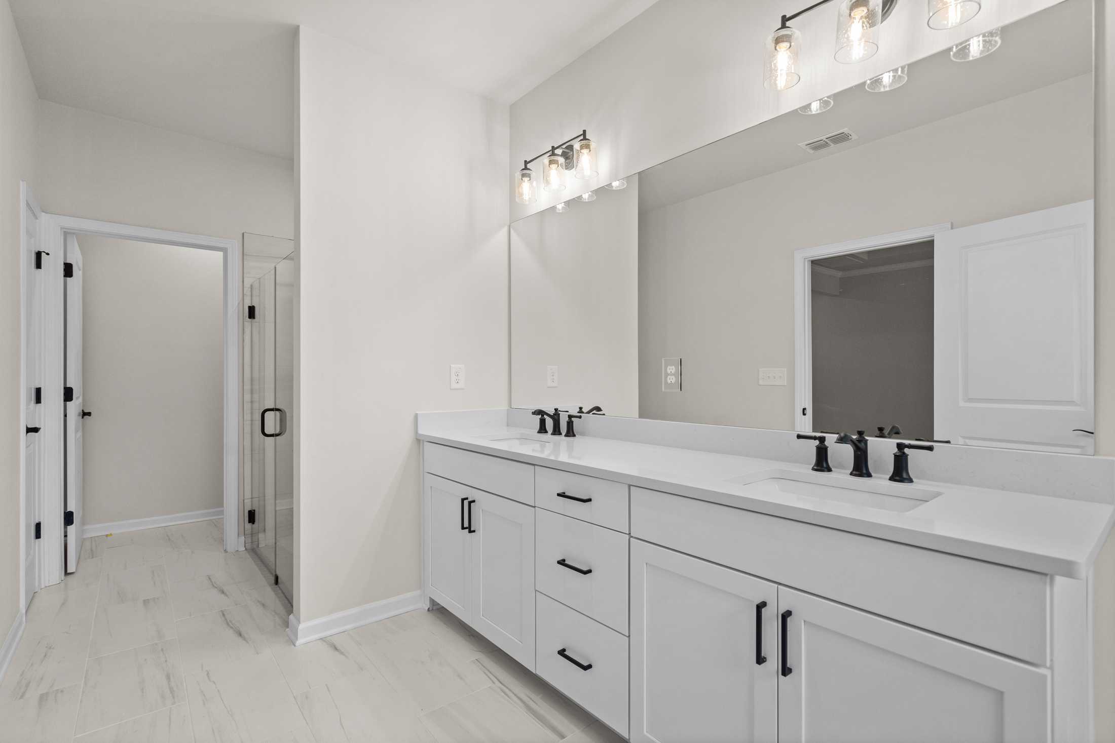 Spacious master bathroom in The Glenwood B featuring white double vanity, large mirror, and glass shower enclosure