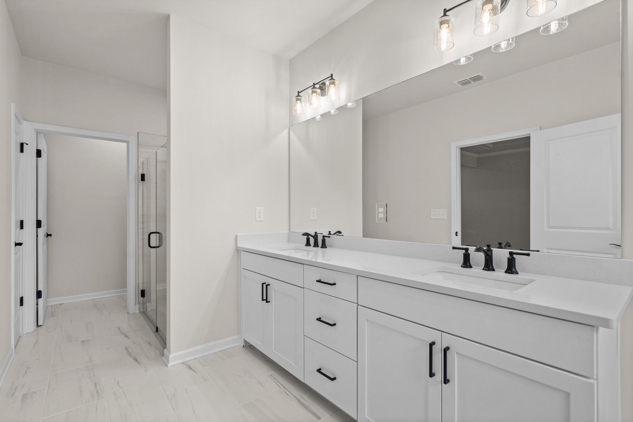 Spacious master bathroom in The Glenwood with white double vanity, large mirror, and frameless glass shower