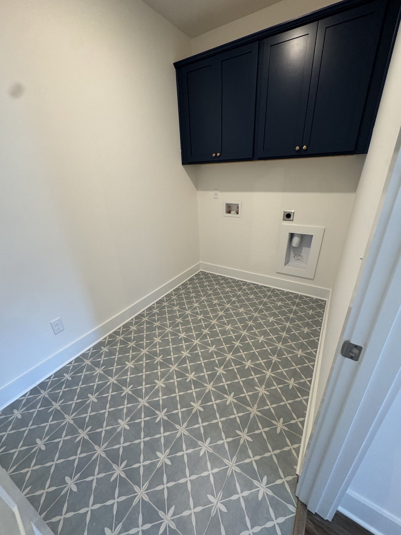 Modern laundry room featuring navy upper cabinets, gray diamond tile floor, and utility sink in Davidson Homes The Ridgeport, Gallatin, TN