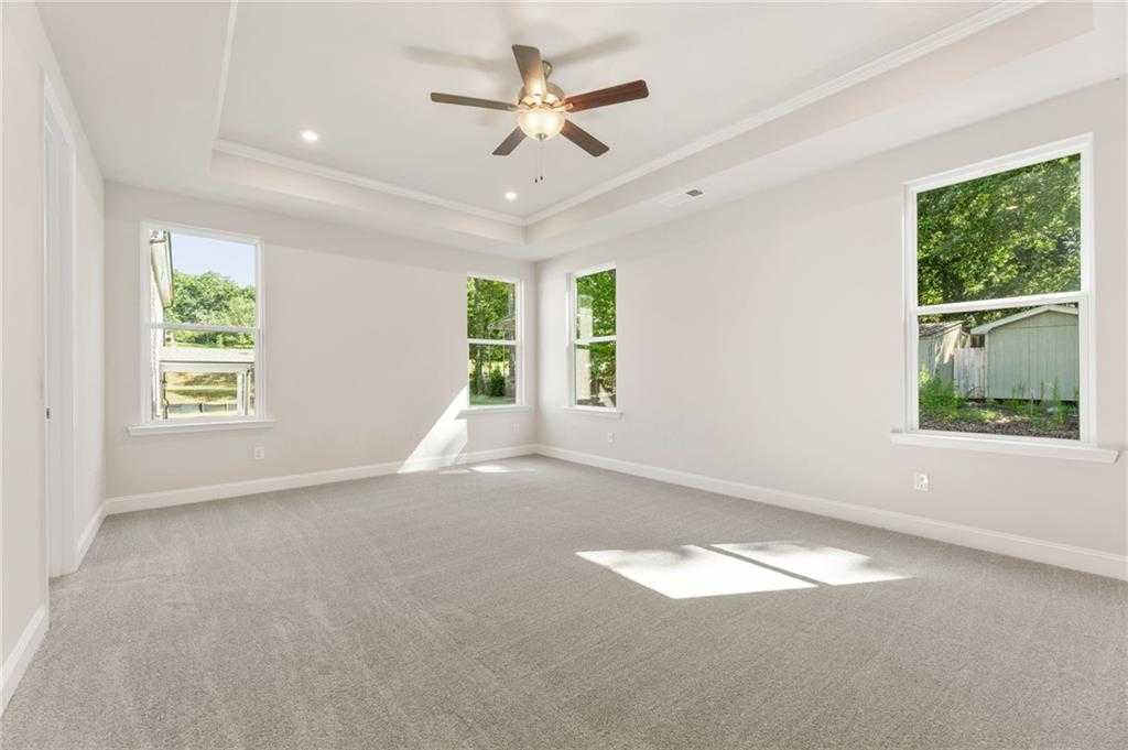 Bright bedroom with tray ceiling, ceiling fan, and large windows overlooking greenery in Davidson Homes The Danbury E, Buford, GA