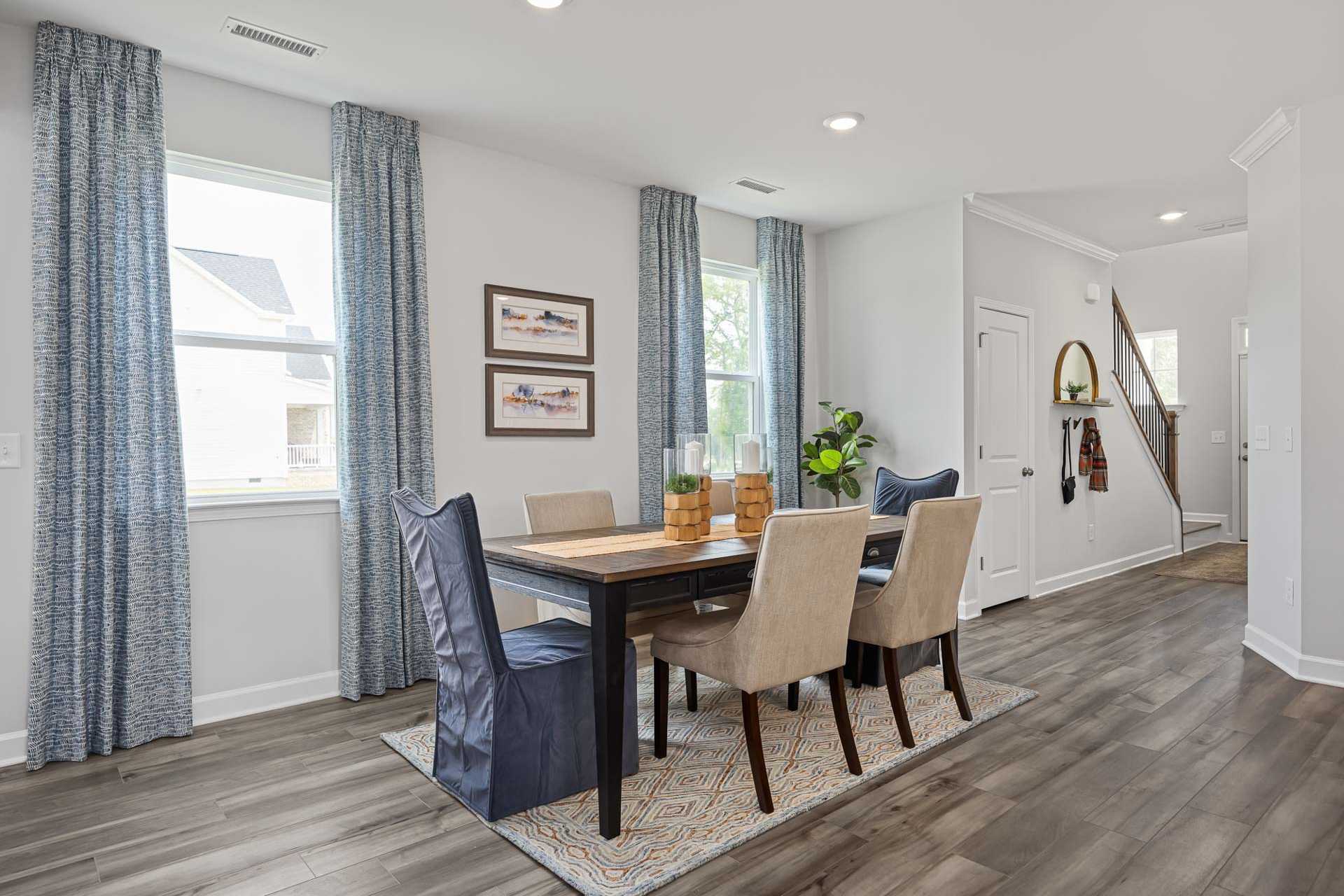 Spacious dining room in Beverly Place, Four Oaks NC by Davidson Homes with wooden table, blue curtains, and hardwood floors