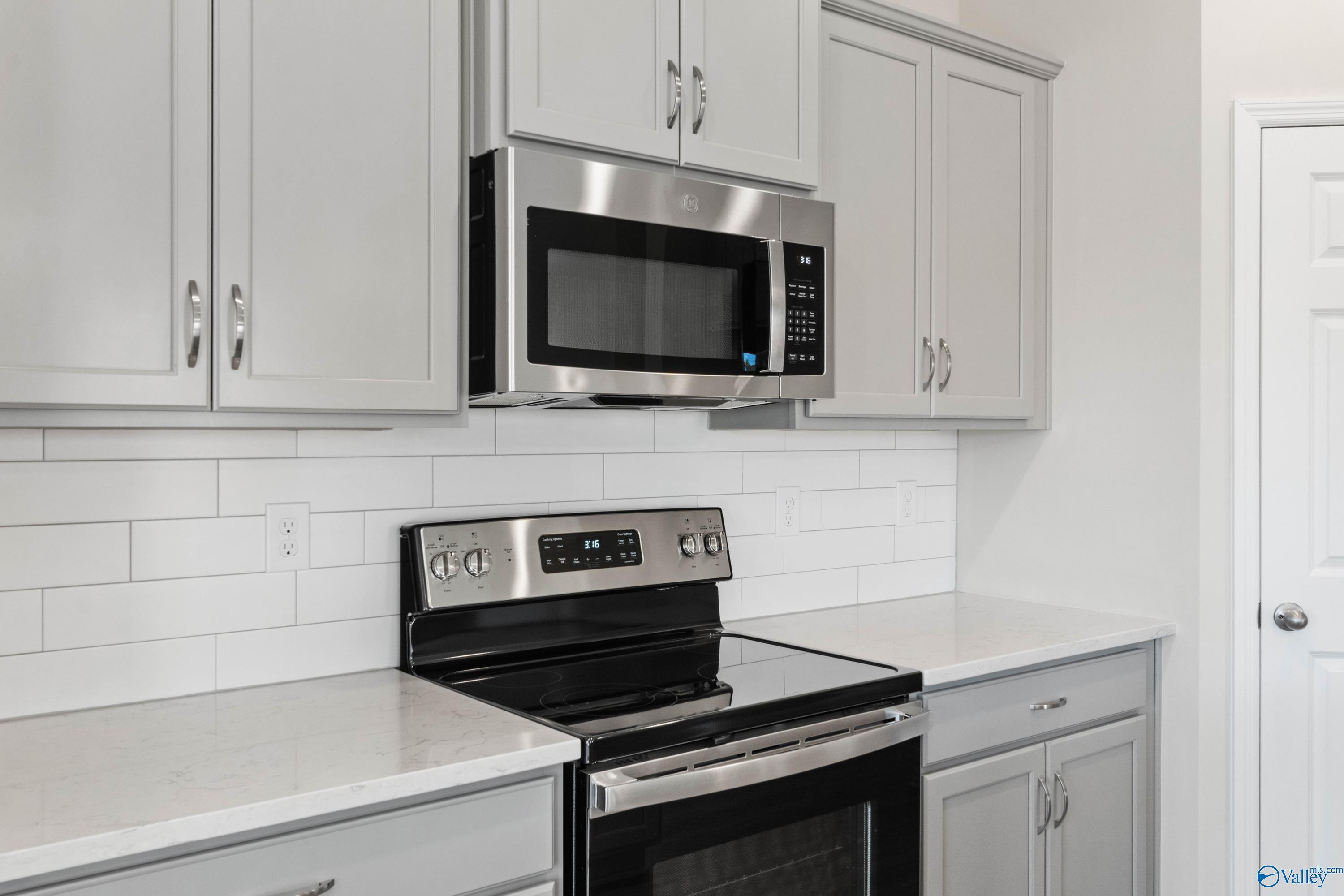 Modern kitchen featuring gray shaker cabinets, white subway tile backsplash, quartz countertops, stainless steel range and microwave in The Franklin C, Athens, AL