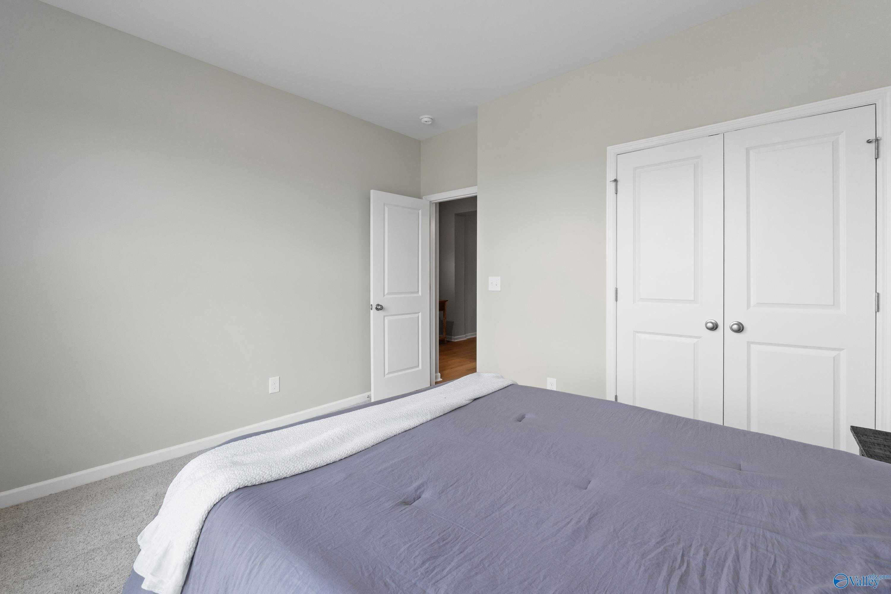 Cozy bedroom featuring gray walls, white double closet doors, open entry, and purple bedding in Davidson Homes The Luna, Hazel Green, Alabama