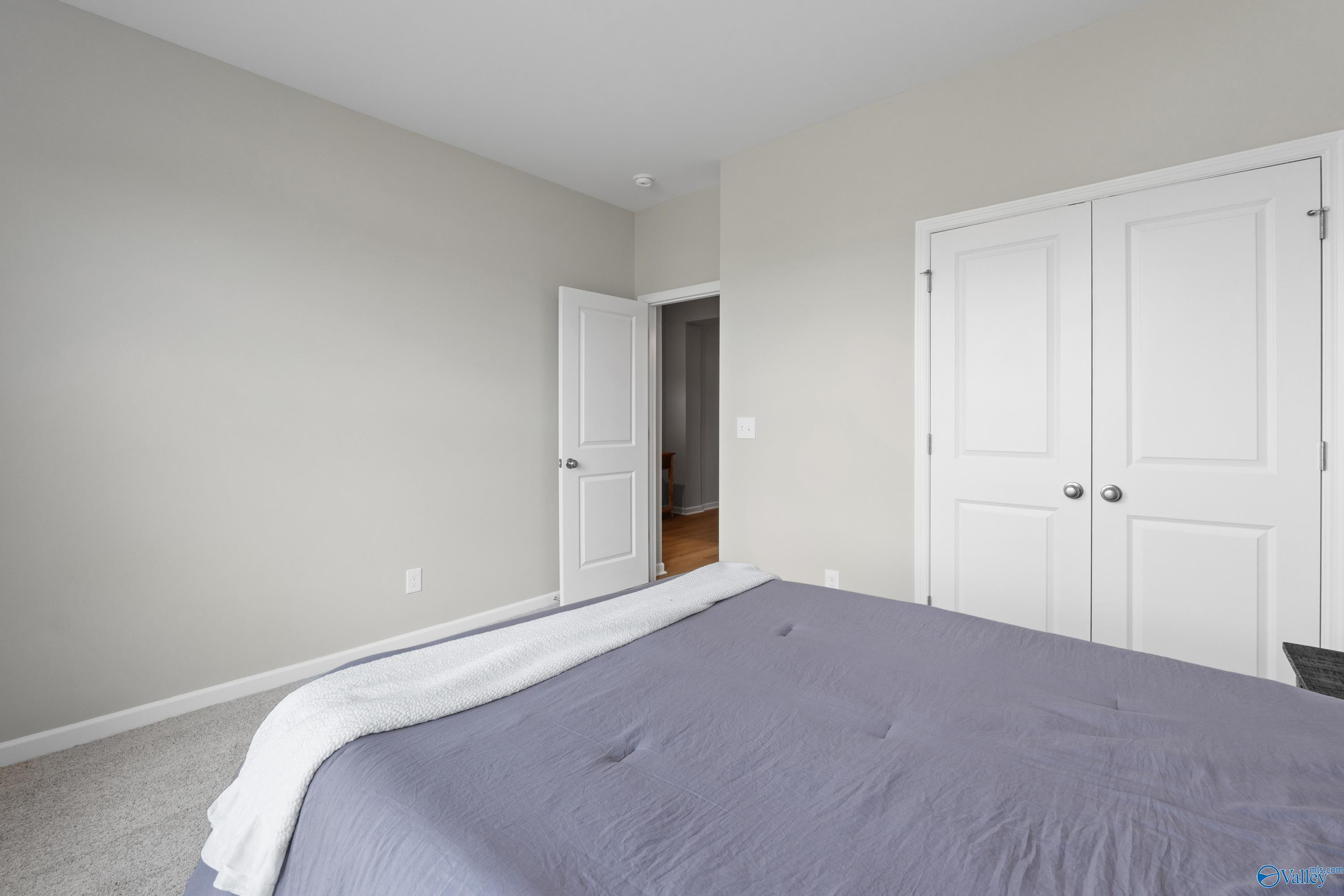 Cozy guest bedroom with light gray walls, white double closet doors, open doorway, and plush purple bed in Davidson Homes The Luna, Hazel Green, Alabama