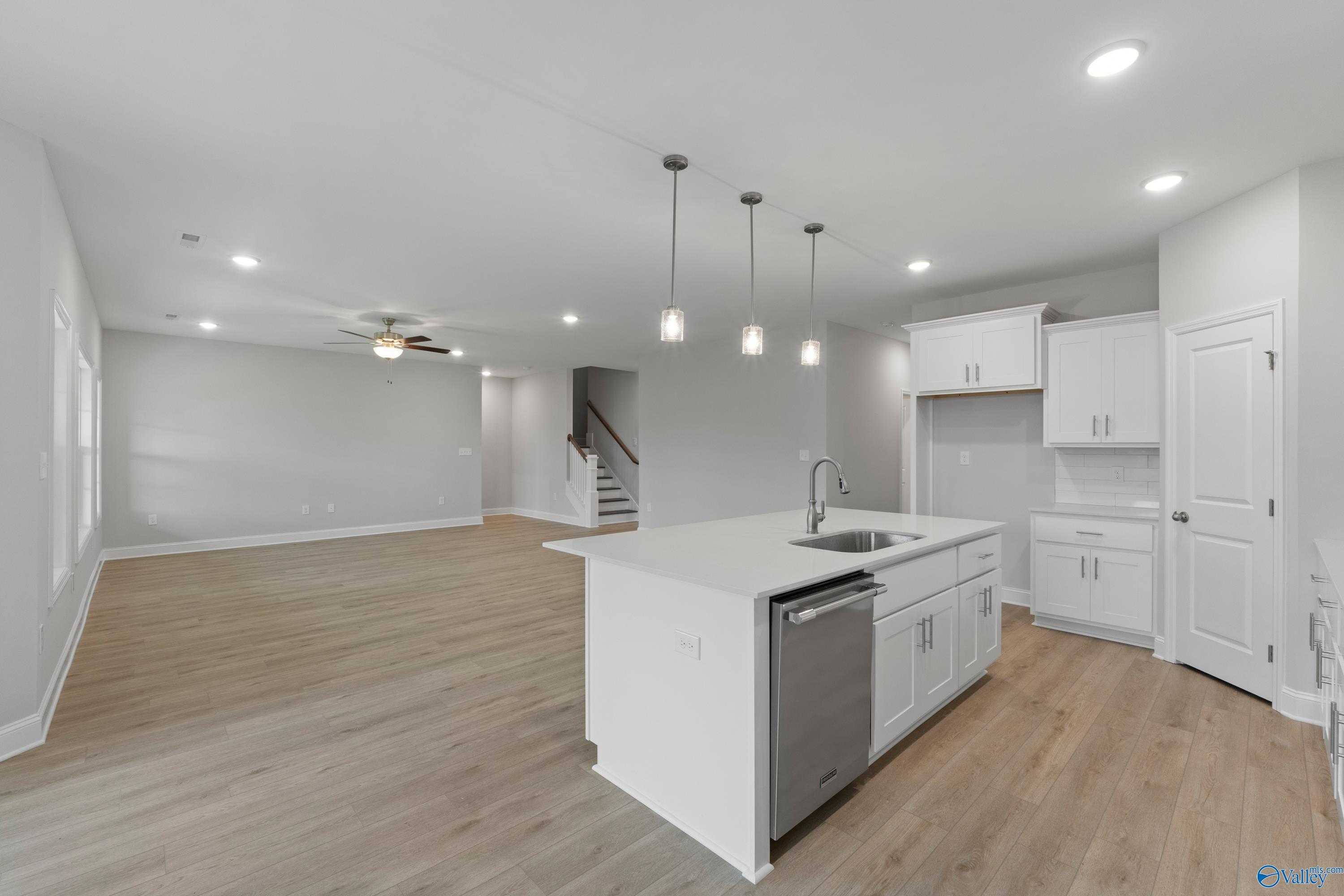 Modern open-concept kitchen with white island sink, stainless dishwasher, hardwood floors, and staircase in Davidson Homes The Rockford B, Toney, Alabama