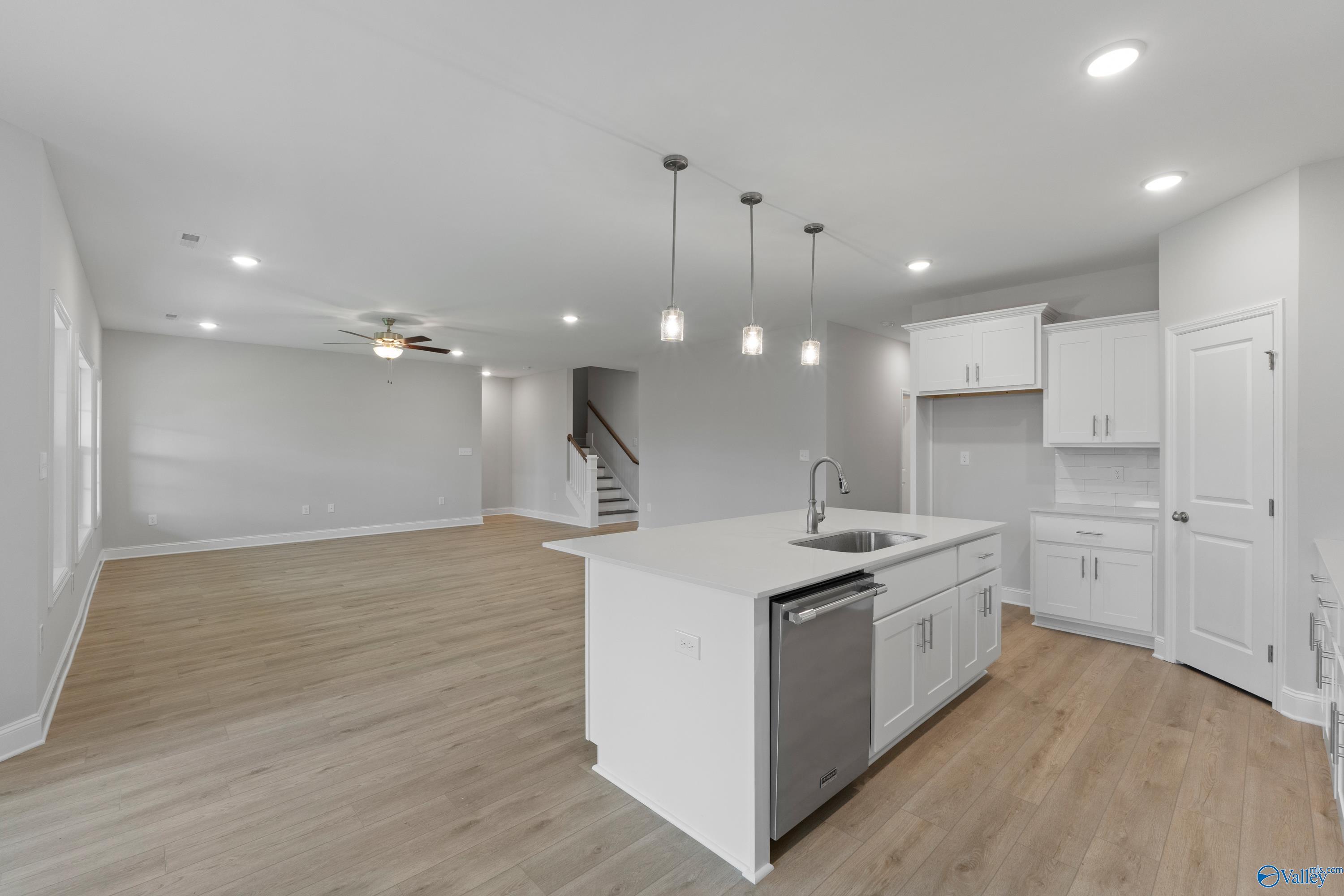 Open-concept kitchen with white island sink, stainless dishwasher, hardwood floors, and staircase in Davidson Homes The Rockford B, Toney, Alabama