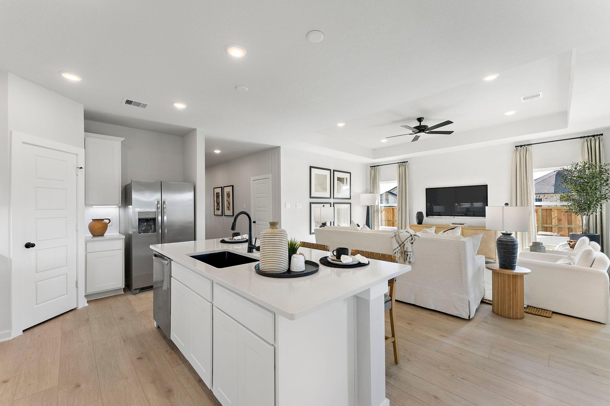 Open-concept kitchen and living room in Sundance Cove, Crosby TX by Davidson Homes featuring white island, hardwood floors, ceiling fan