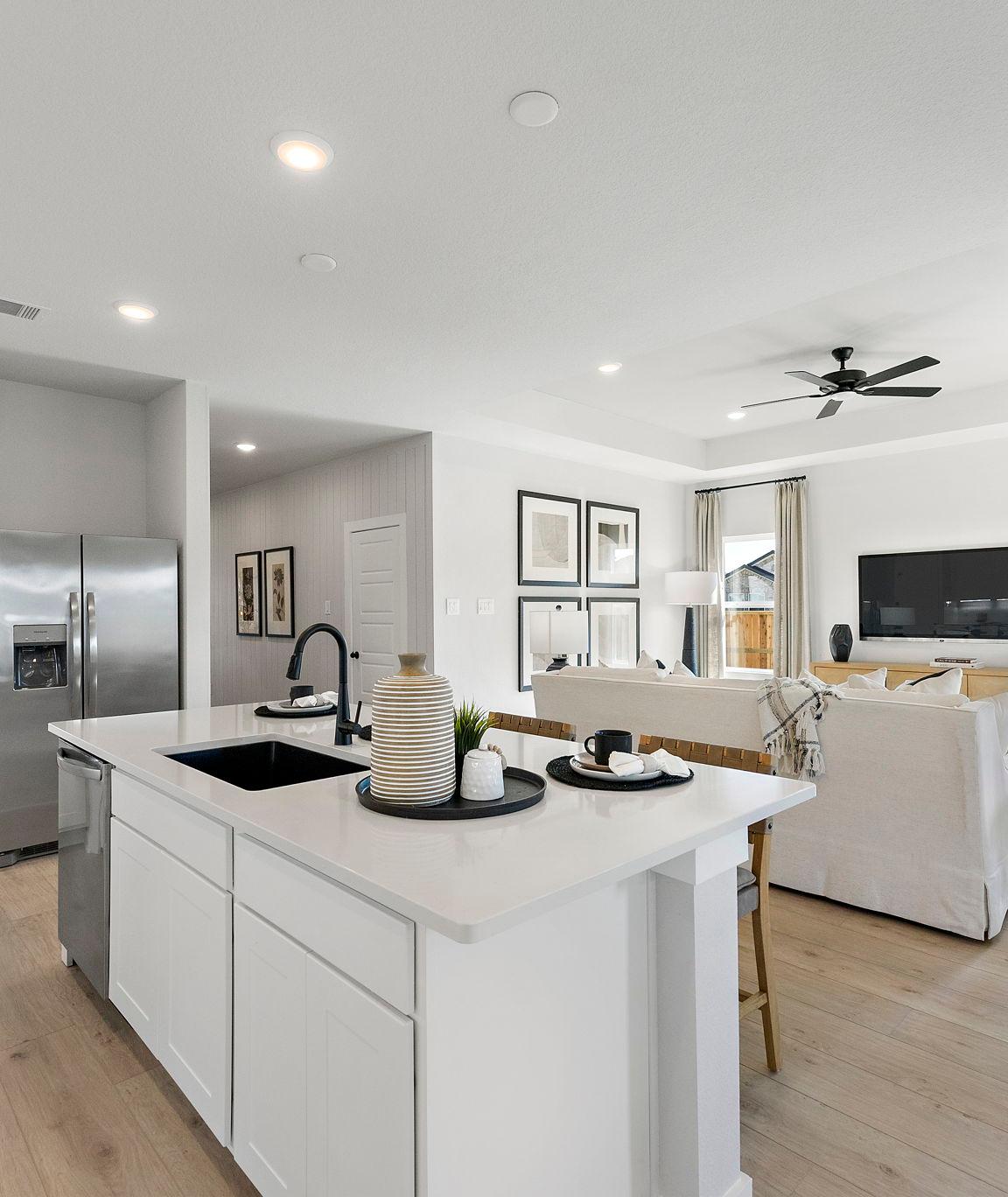 Open-concept kitchen and living room in Sundance Cove Crosby Texas with white island, hardwood floors, ceiling fan and modern white seating