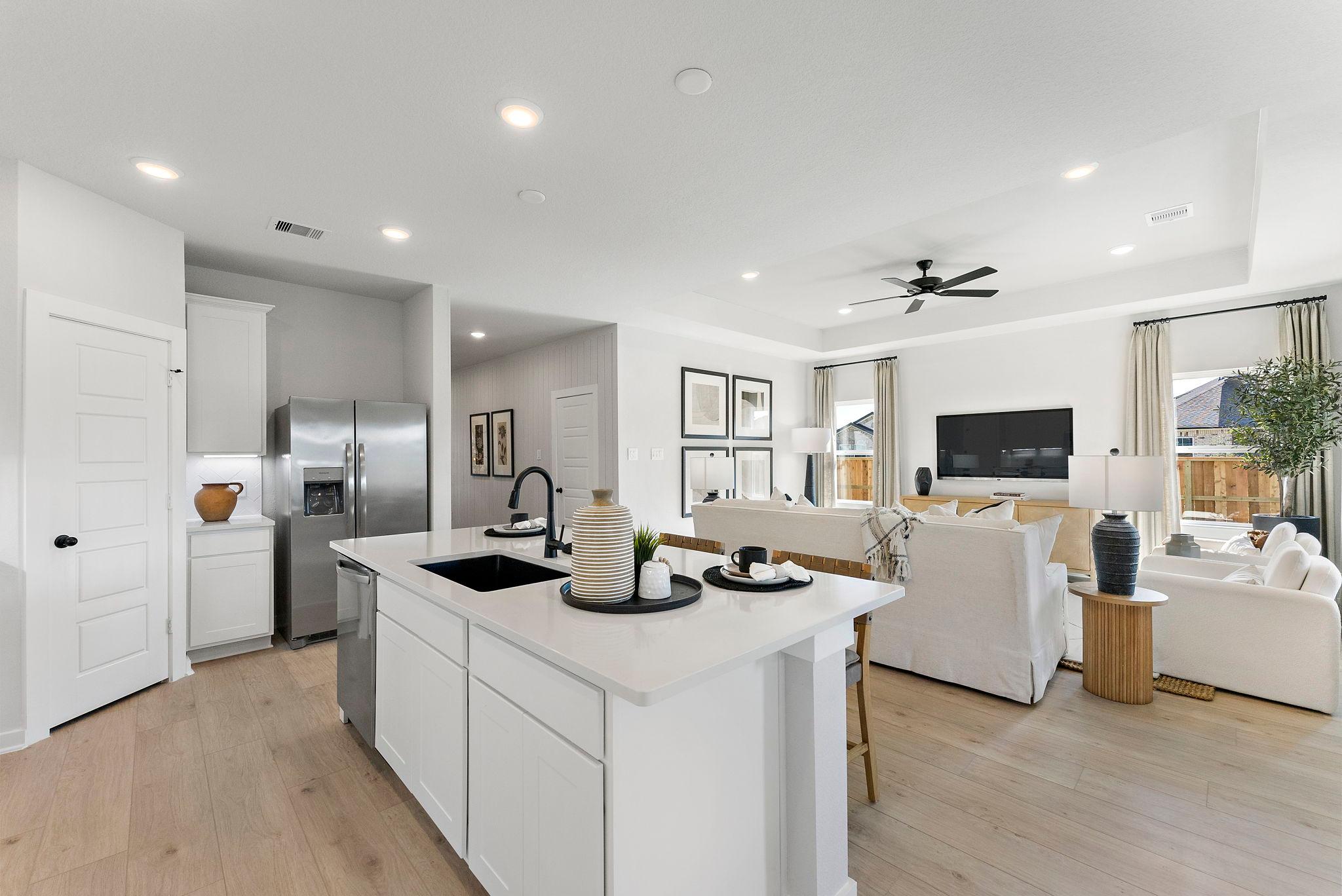 Open-concept kitchen and living room in Sundance Cove Crosby Texas with white island, hardwood floors, ceiling fan and modern white seating