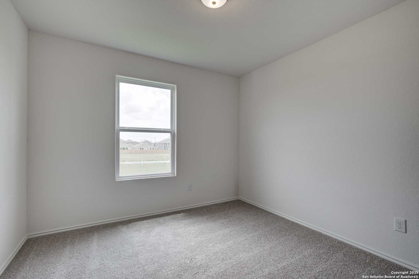 Empty bedroom with neutral gray walls, carpet flooring, and large window in Davidson Homes The Trinity A, San Antonio, Texas