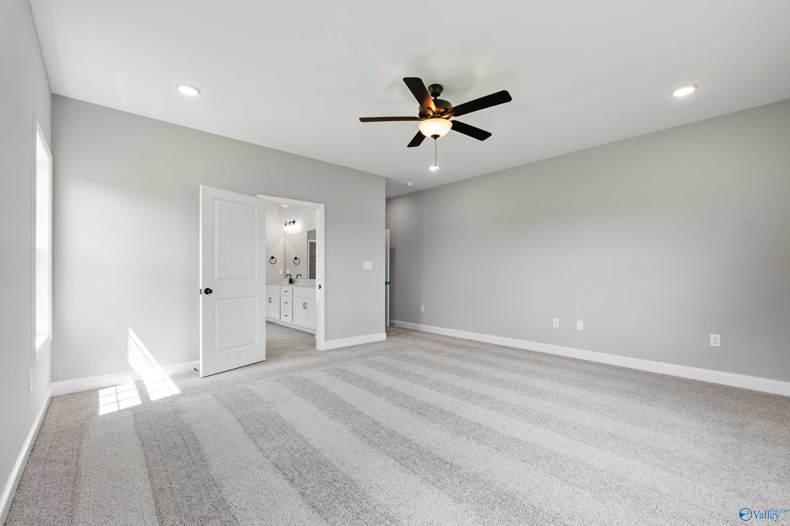 Spacious gray bedroom with ceiling fan, carpeted floors, and en-suite bathroom in Davidson Homes The Finleigh, Toney, AL