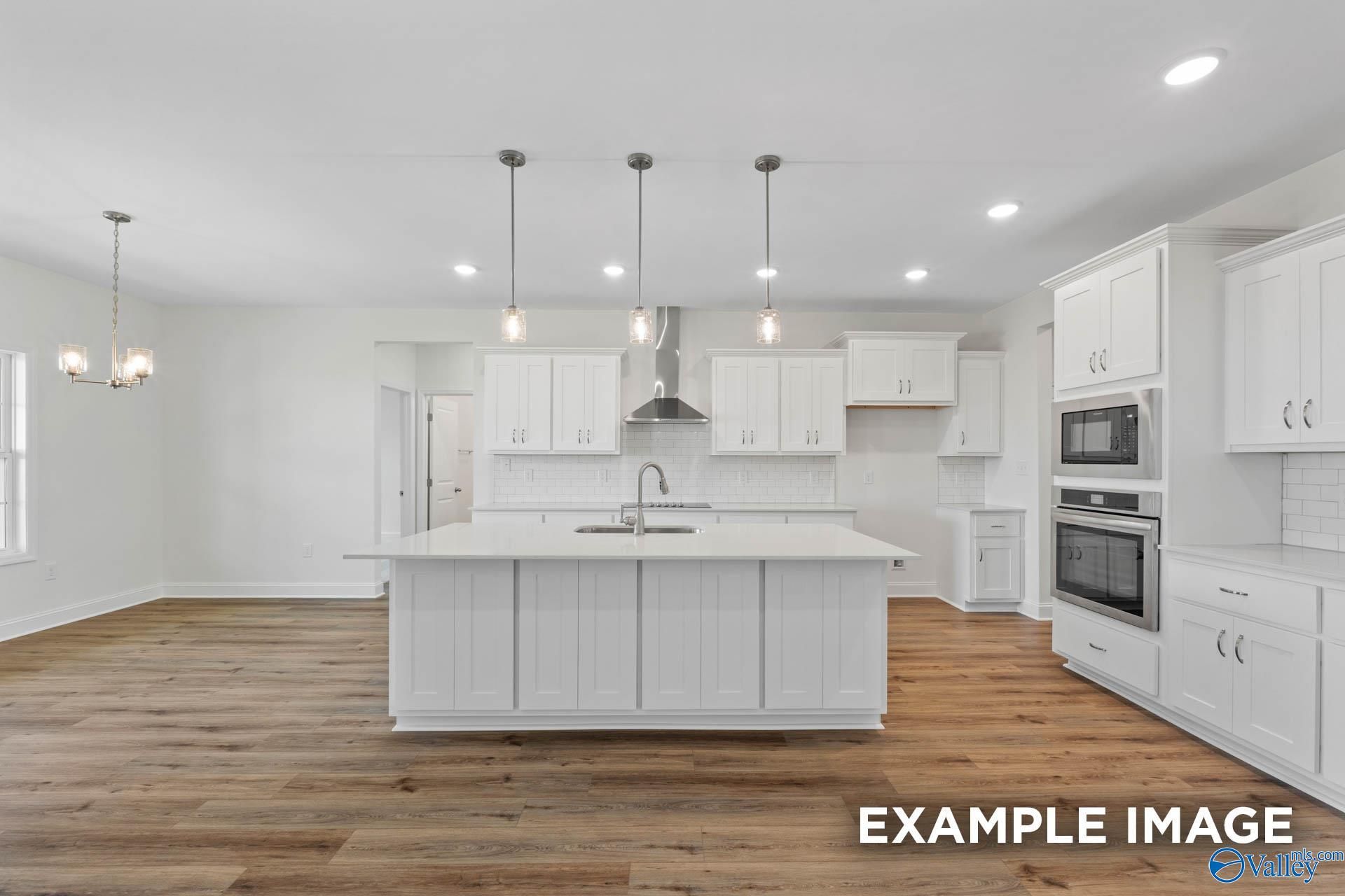 Modern white kitchen island with stainless double oven, pendant lights, and hardwood floors in Davidson Homes The Oxford, Huntsville AL