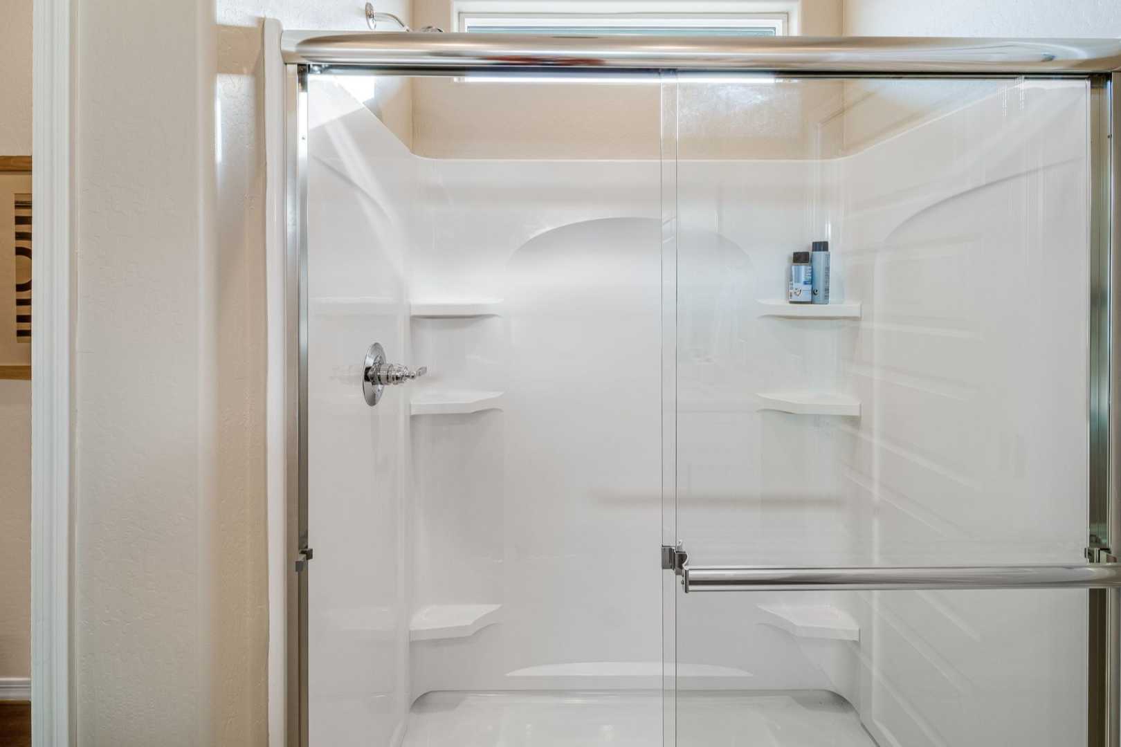 Spacious walk-in shower in The Newport B master bath with glass enclosure, white tile surround, built-in bench and shelves
