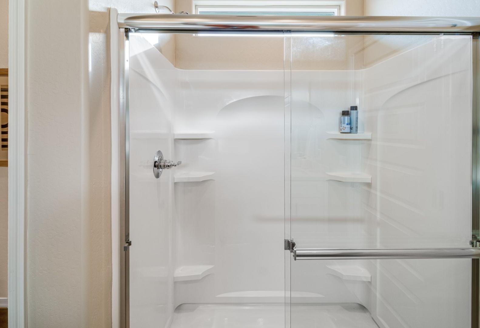 Spacious walk-in shower in The Newport A master bathroom with glass doors, white tile, and built-in shelves