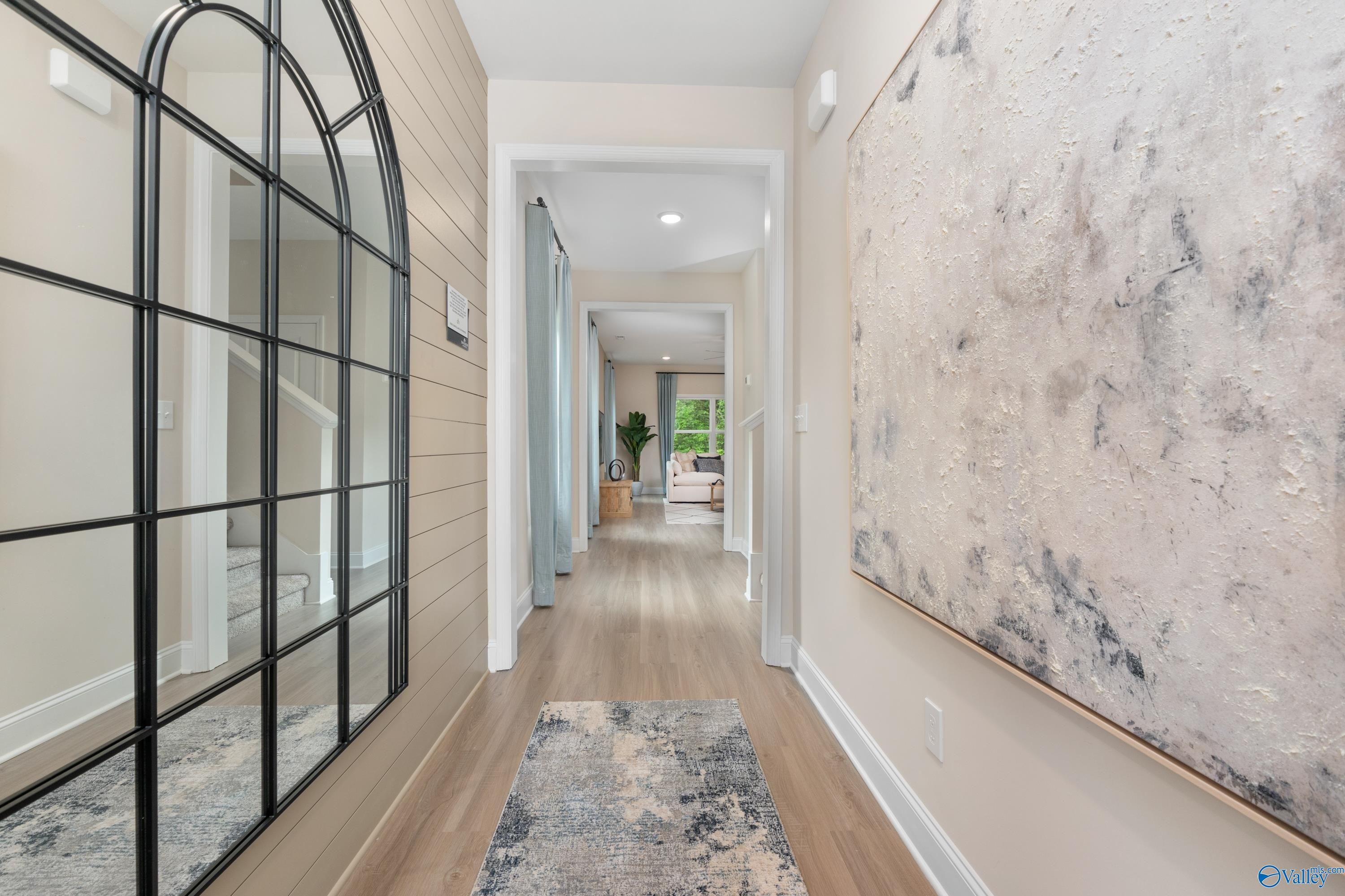 Elegant entry hallway with arched black mirror, abstract art, wood floors in Davidson Homes The Camden, Huntsville AL