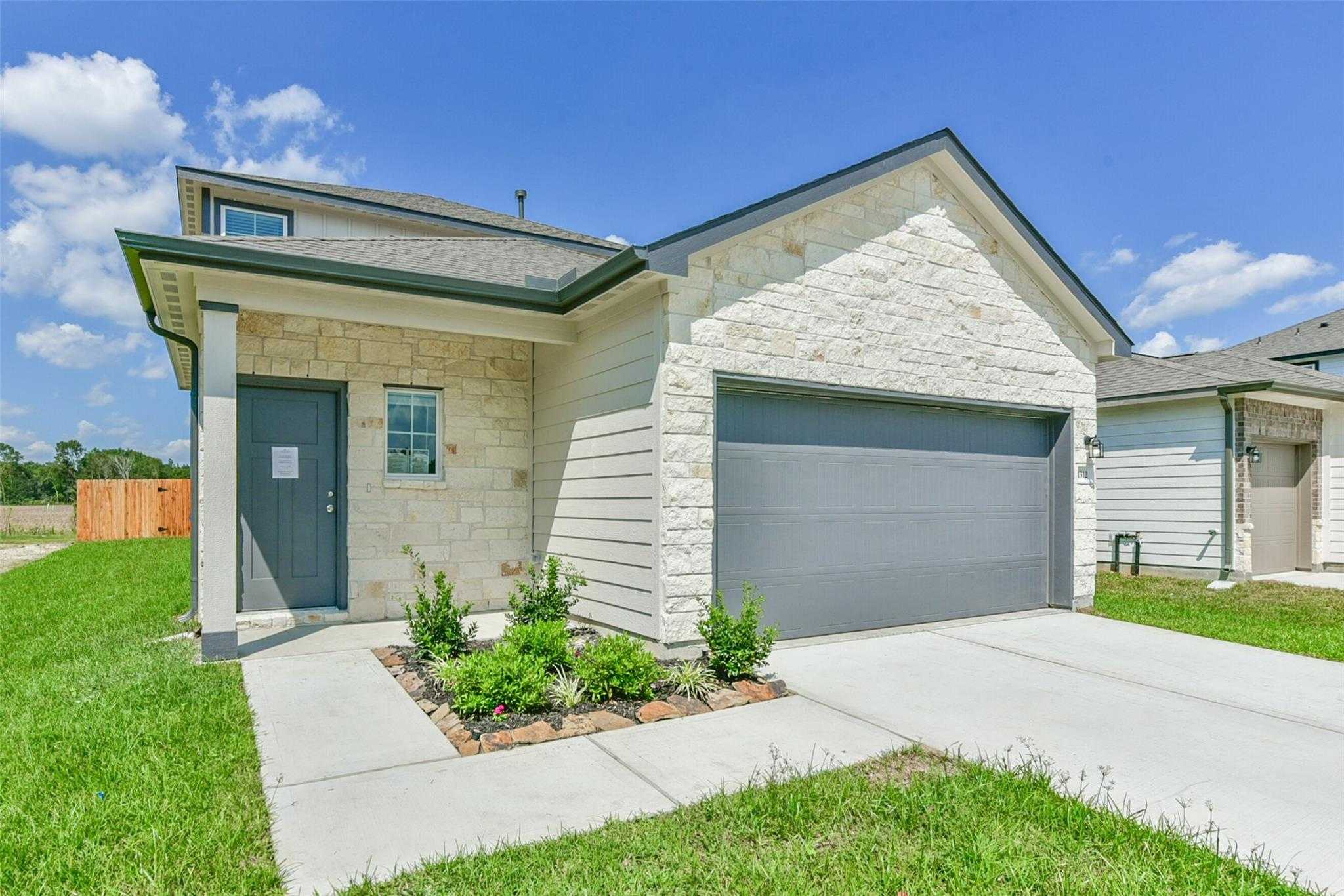 Modern 2-story stone facade home with 2-car garage, covered porch, and landscaped yard in The Villages at WestPointe, Dayton, Texas