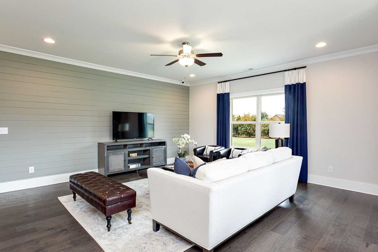 Spacious living room at Williams Pointe in Huntsville AL featuring white sectional sofa, gray shiplap walls, hardwood floors, and navy curtained windows