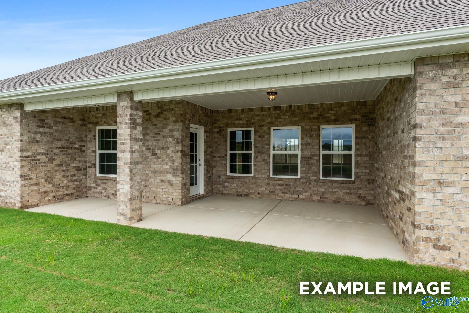 Covered back patio with brick walls, large windows, columns, and lush green lawn in Davidson Homes The Emory, Toney, Alabama