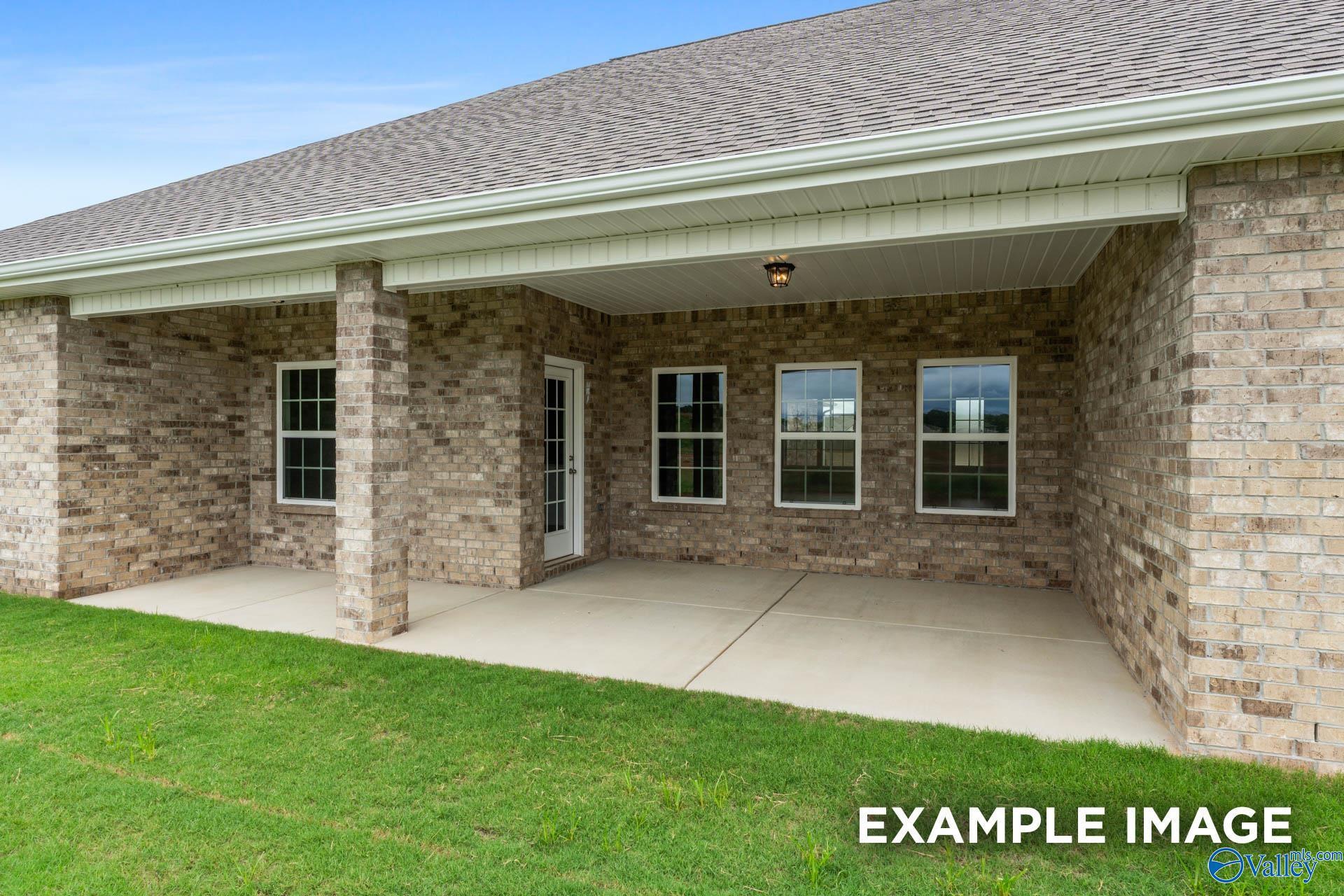 Covered back patio with brick walls, large windows, columns, and lush green lawn in Davidson Homes The Emory, Toney, Alabama
