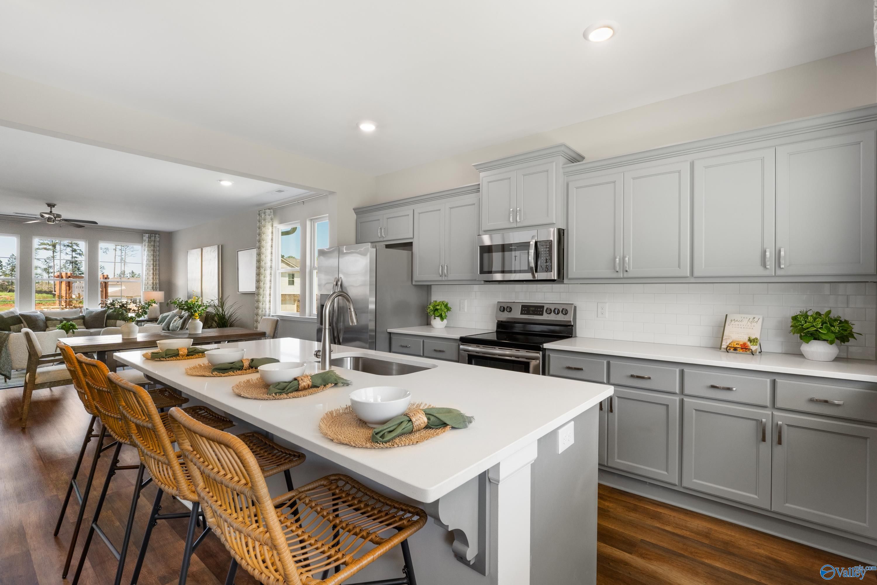 Modern open kitchen with gray shaker cabinets, white quartz island, rattan stools, stainless appliances in Davidson Homes The Stella, Madison AL