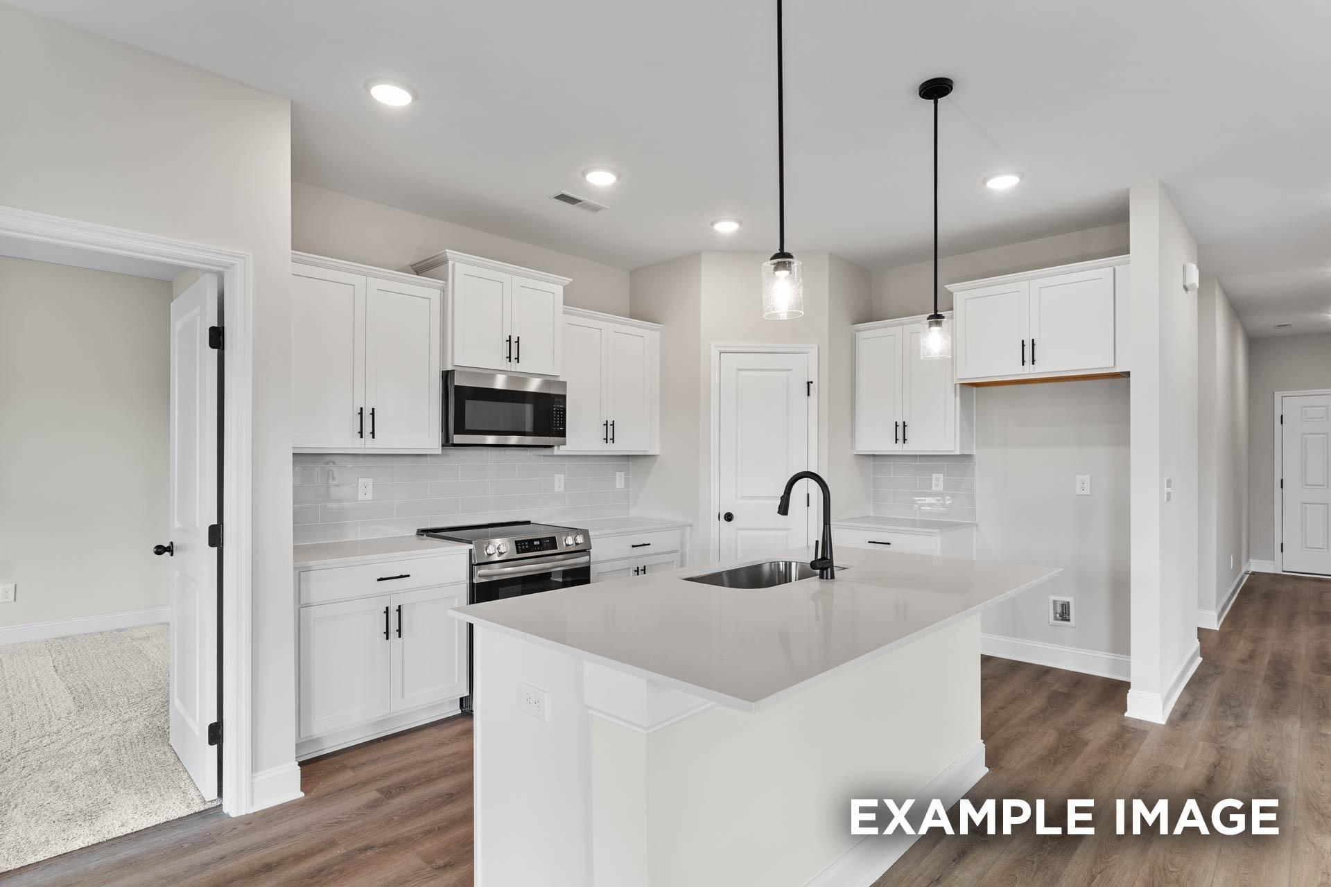 Modern kitchen with white cabinets, quartz island, and stainless steel appliances in The Franklin E home in Bailey Park.