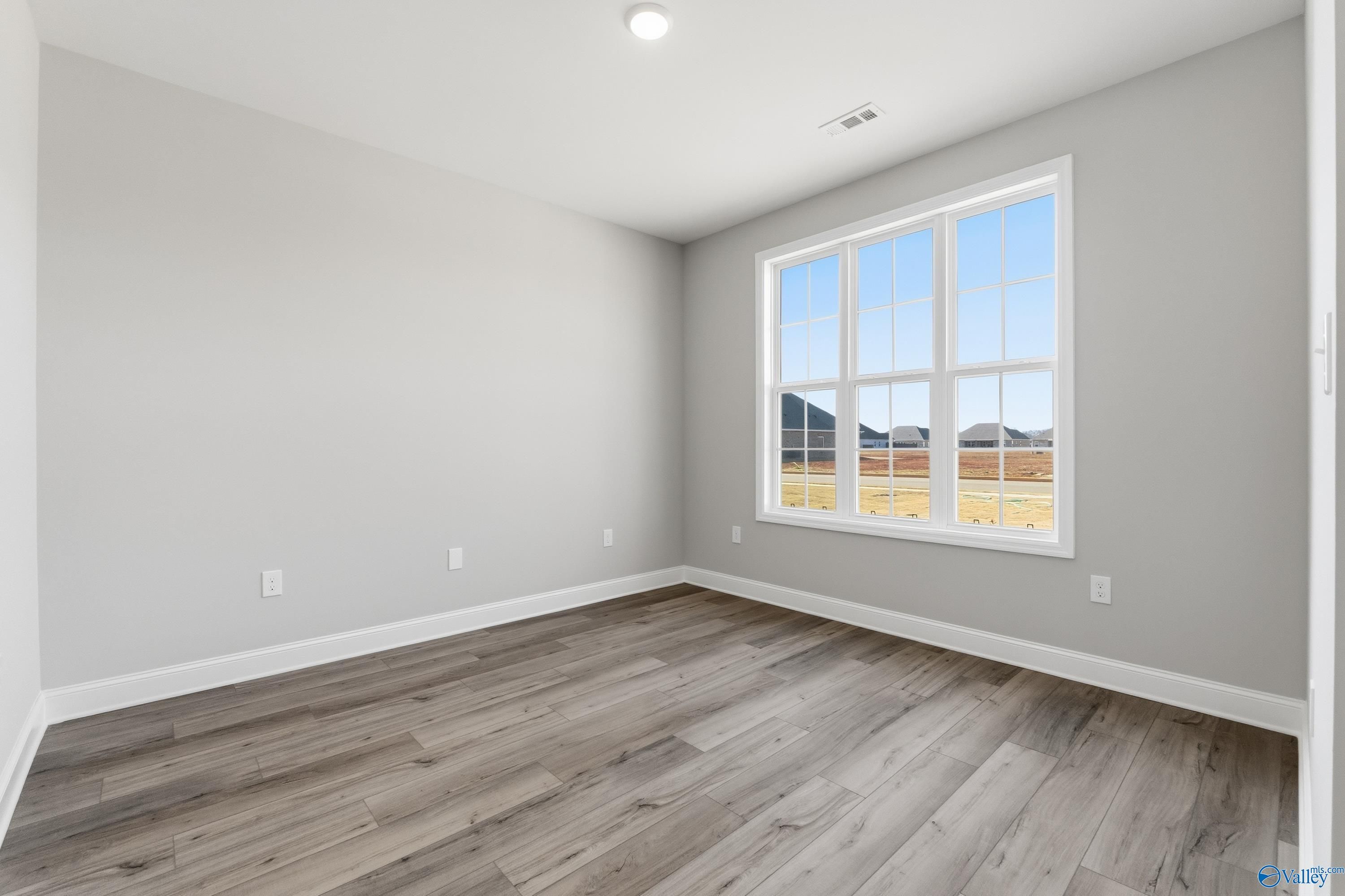 Bright secondary bedroom with large triple-window overlooking scenic fields, gray walls, and hardwood floors in Davidson Homes Finleigh, Meridianville AL