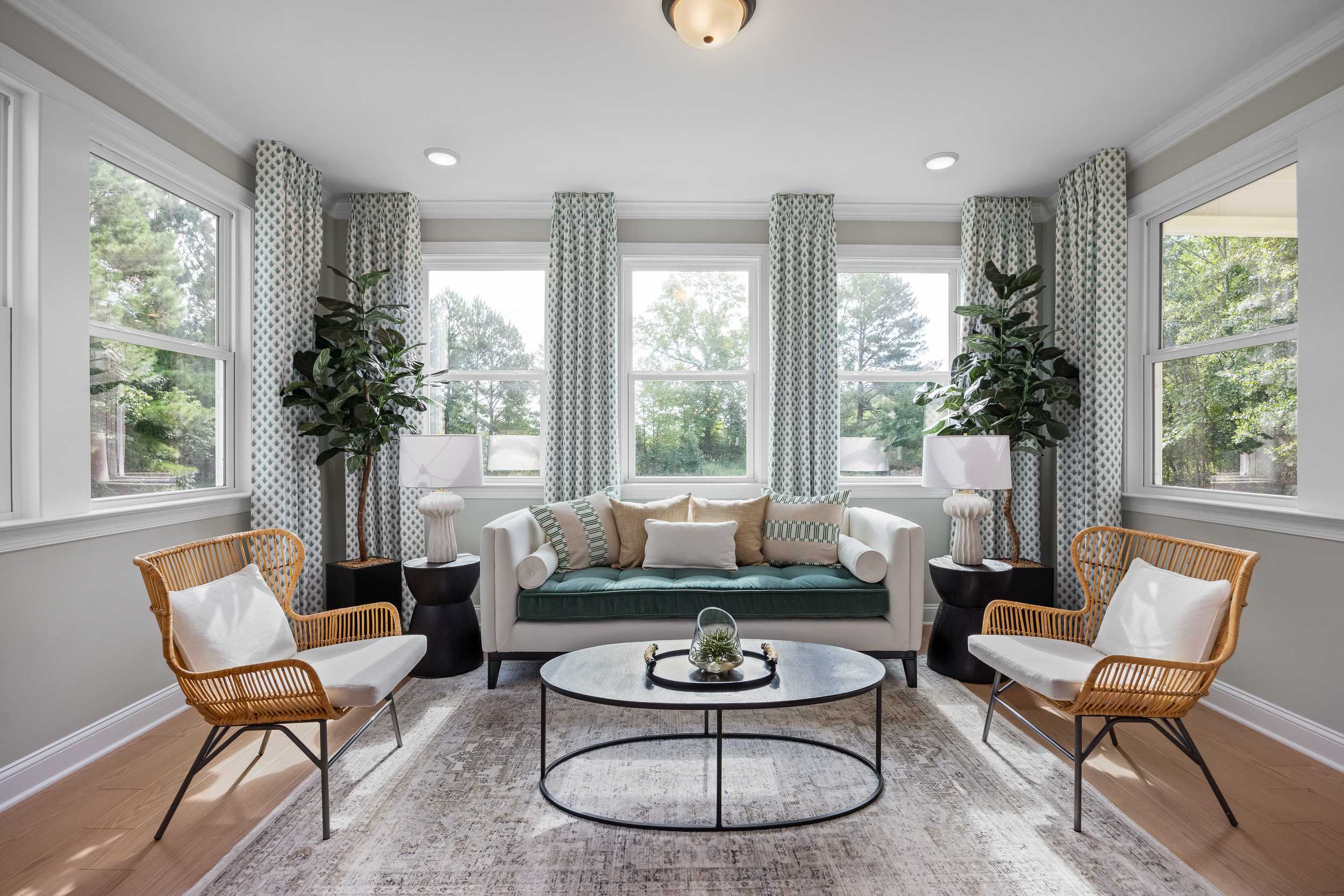 Bright sunroom with large windows, potted palms, beige sofa, rattan chairs and coffee table at Laneridge Estates Raleigh NC