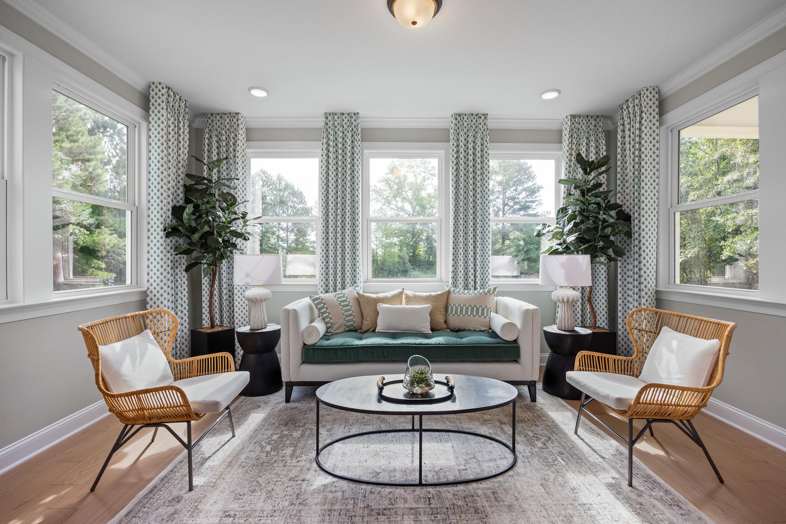 Bright sunroom with large windows, potted palms, beige sofa, rattan chairs and coffee table at Laneridge Estates Raleigh NC