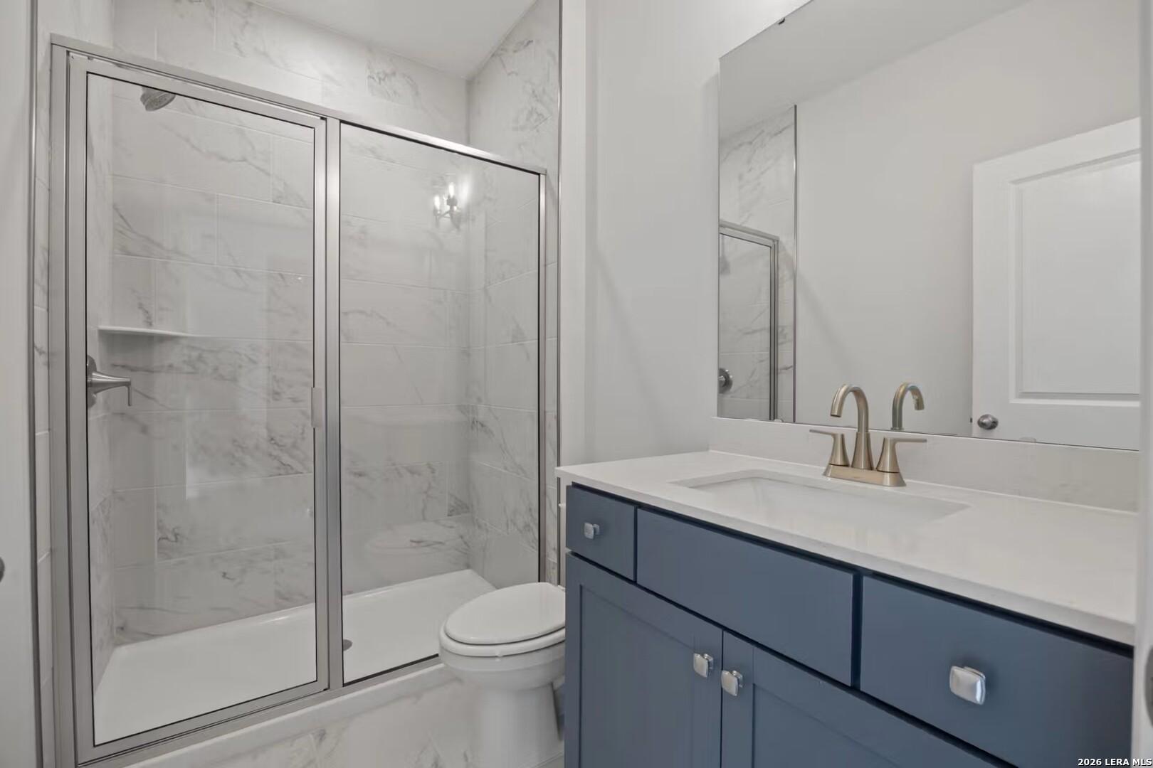 Modern bathroom with marble-tiled walk-in shower and blue vanity in The Ashport F floor plan at Morgan Meadows, San Antonio.