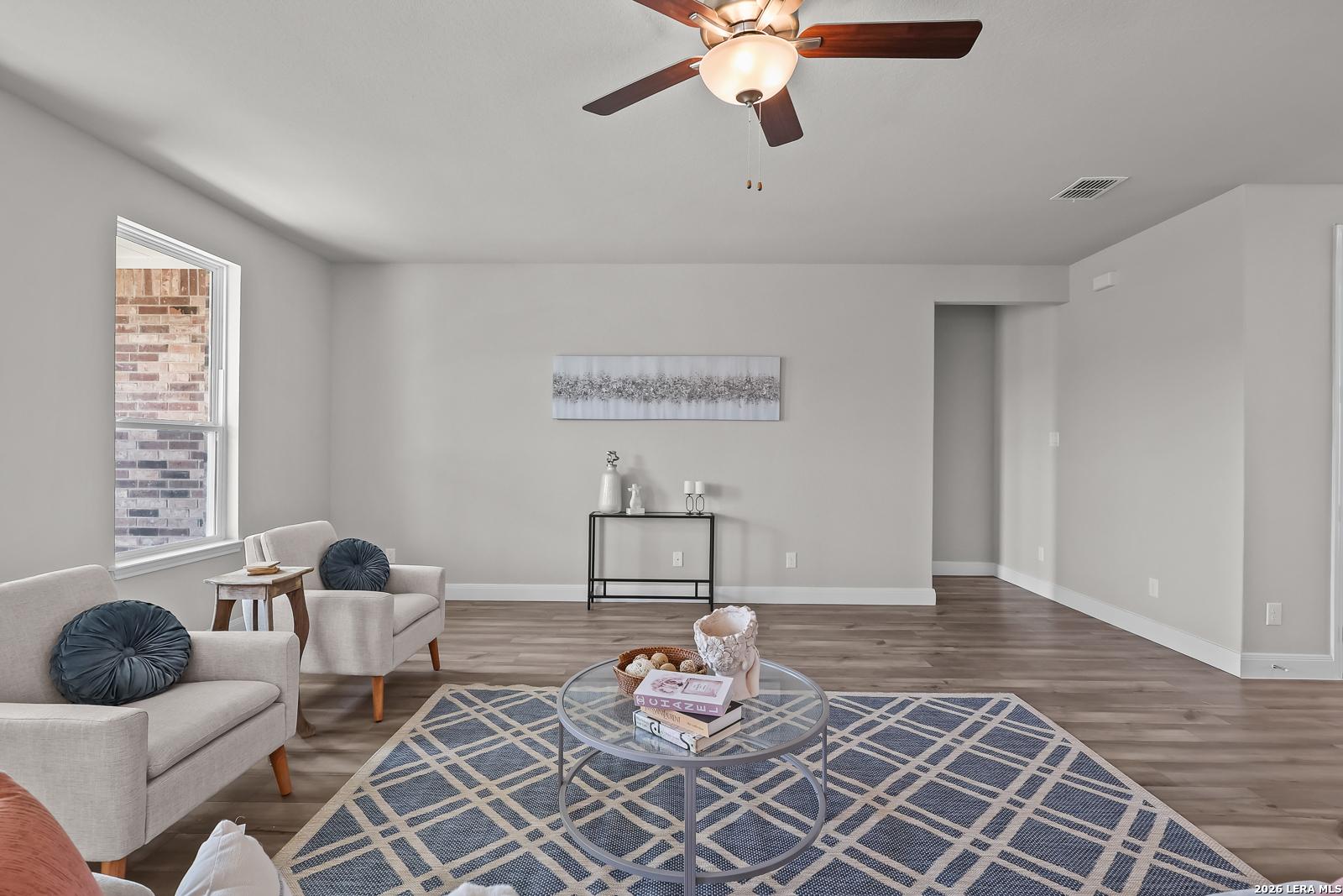 Cozy living room with beige sofa, armchairs, blue patterned rug, and ceiling fan in Davidson Homes The Rockford G, Ladera, San Antonio