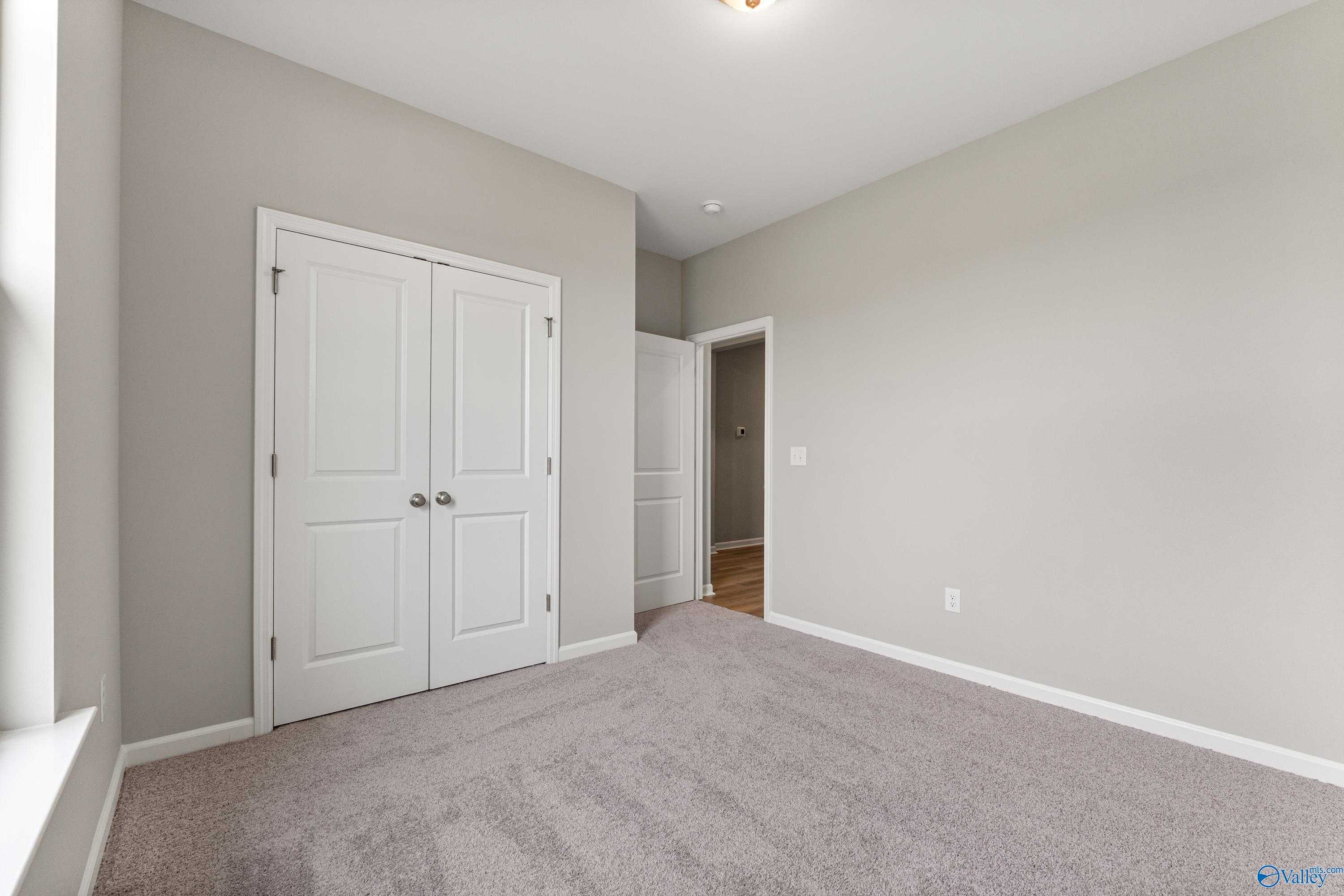 Bright bedroom with light gray walls, white double closet doors, en-suite bathroom entry, and plush carpet in Davidson Homes The Aurora, Fayetteville, TN