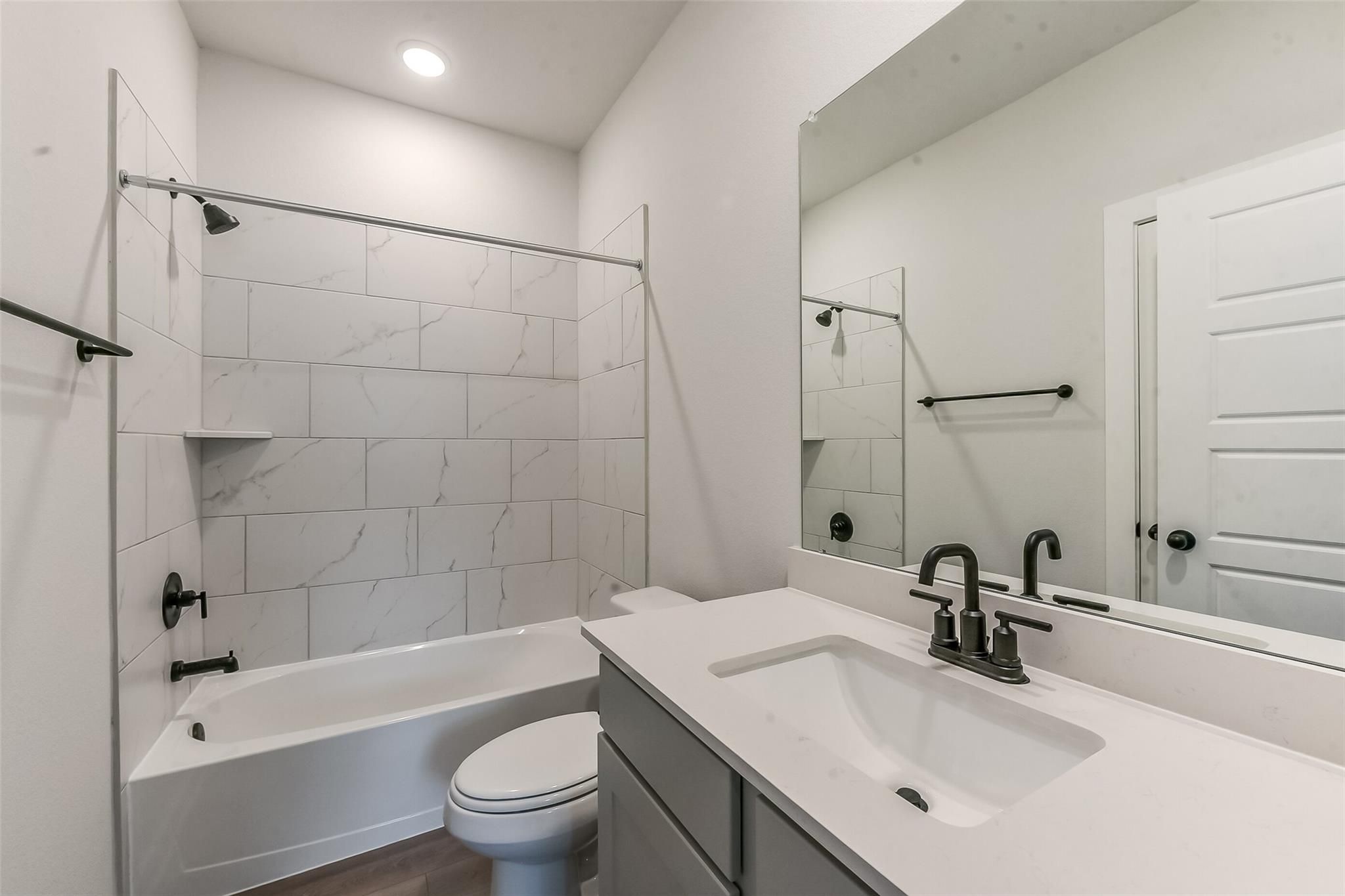Elegant bathroom with white marble-look tile shower, soaking tub, modern black faucet vanity, and toilet in Davidson Homes Everett C, Crosby, Texas