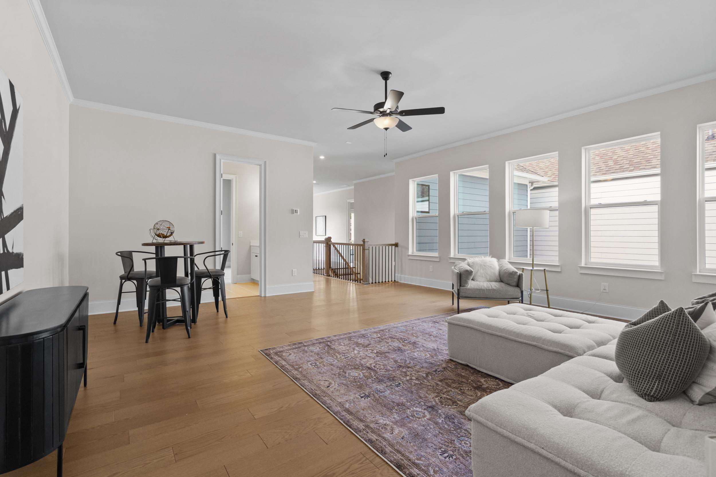 Spacious open-concept living room at The Village at Towne Lake in Woodstock GA with hardwood floors, white sectional sofa, ceiling fan and large windows