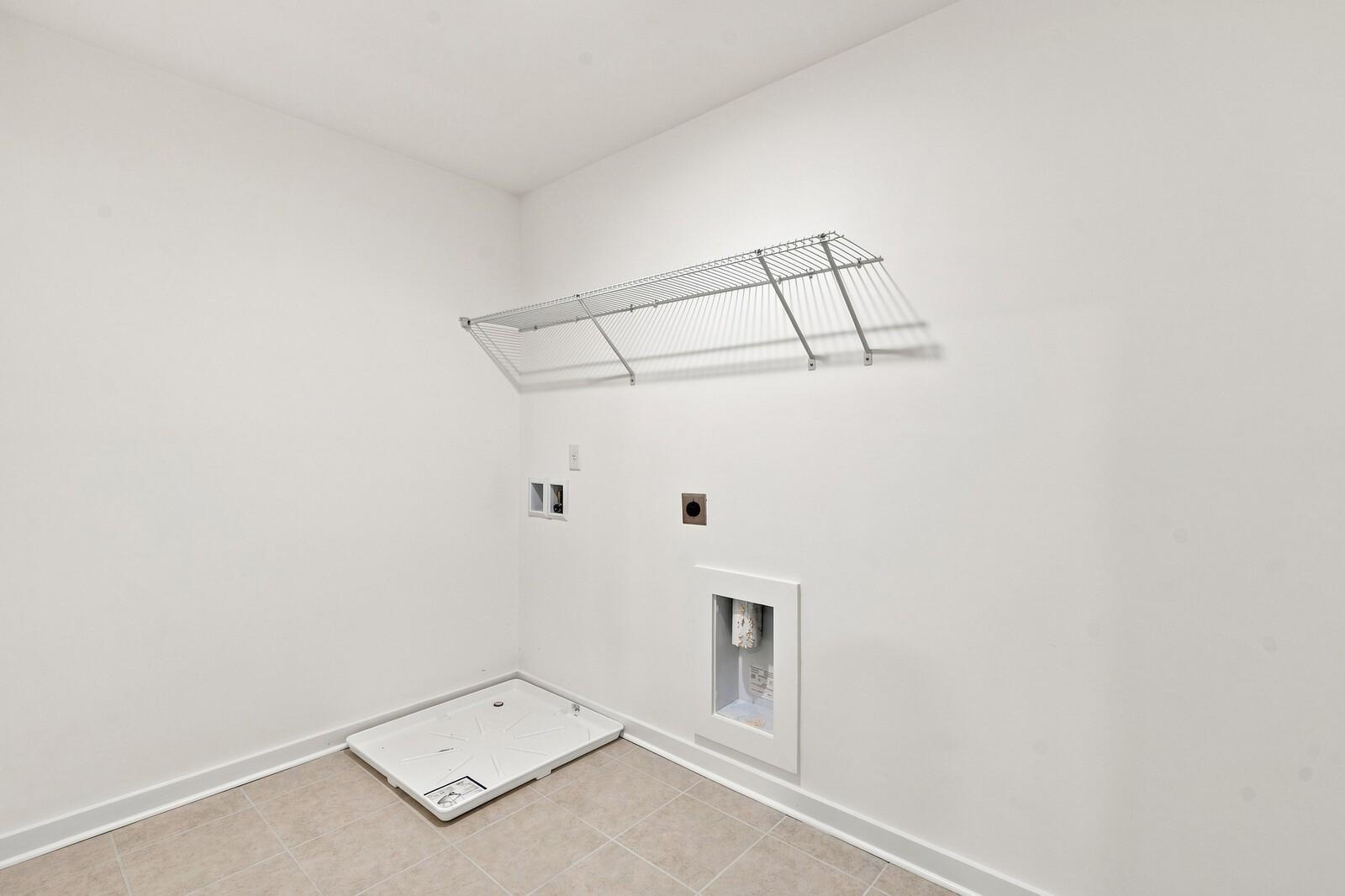 Laundry room with wire shelving, washer drain pan, and tile flooring in Davidson Homes The Willow C, Gallatin, Tennessee