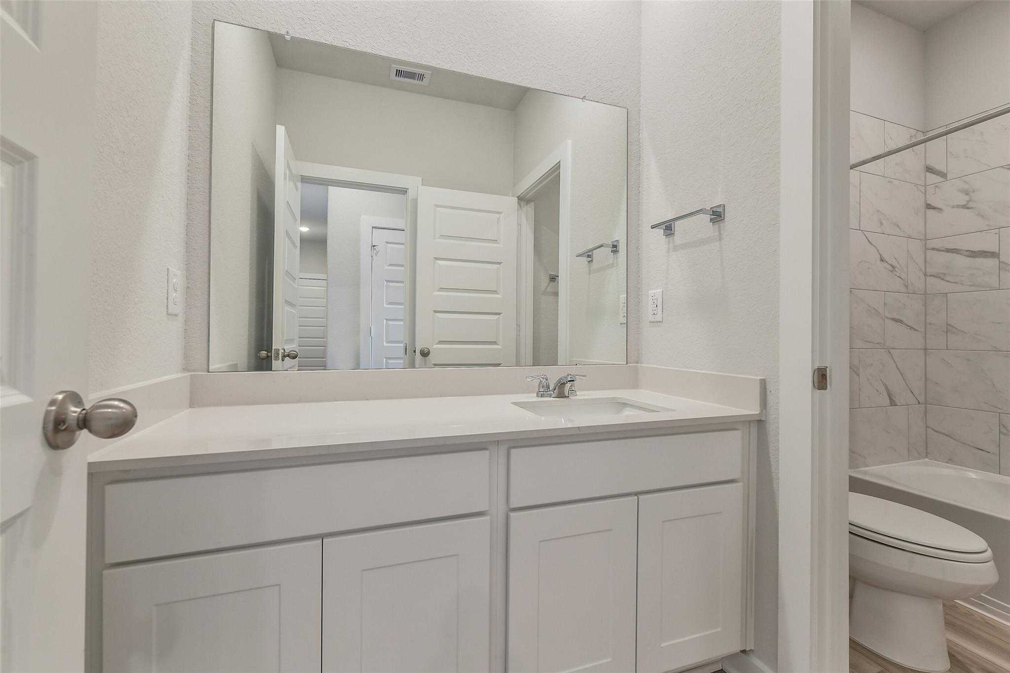 Modern master bathroom with double vanity, large mirror, white shaker cabinets, and tiled shower in Davidson Homes The Colorado G, Magnolia, Texas