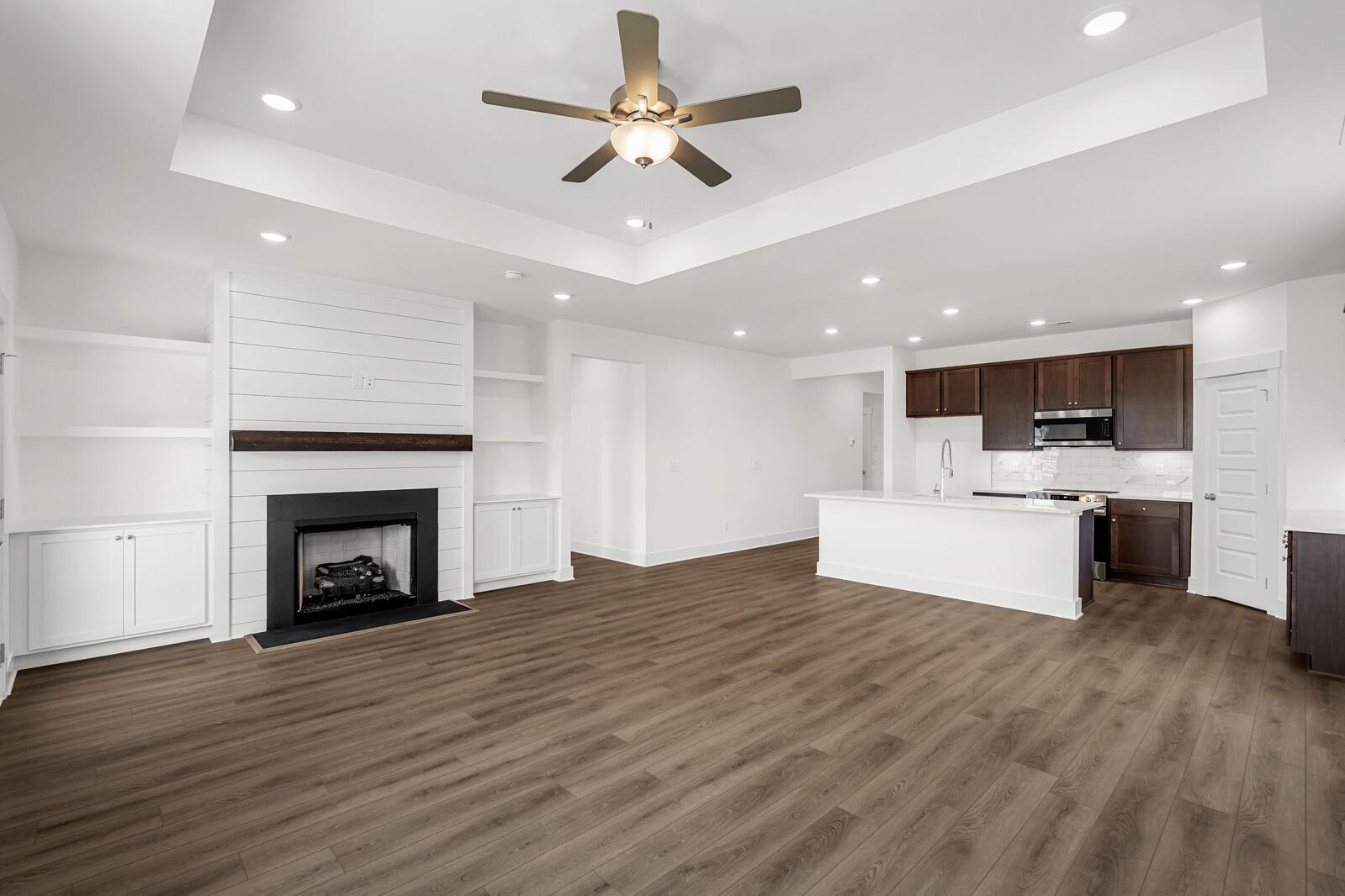Open-concept living area in The Cottonwood featuring a shiplap fireplace, tray ceiling, and kitchen with a large island.
