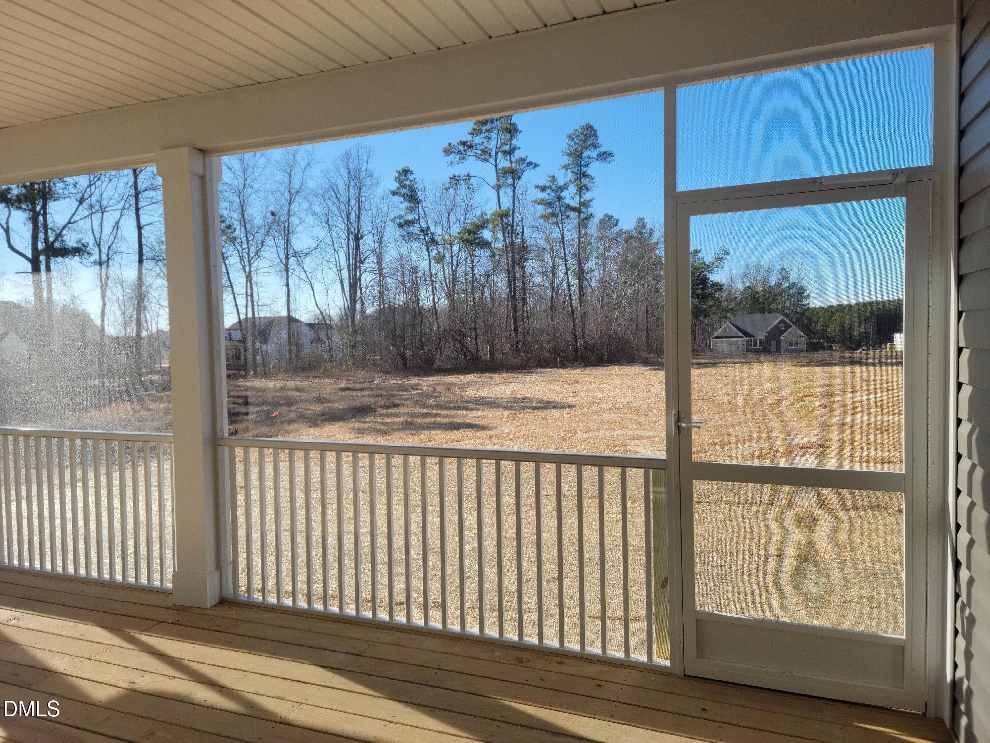 Screened porch with wooden deck, white railing, and views of pines, open field in Davidson Homes The Magnolia B, Angier, NC