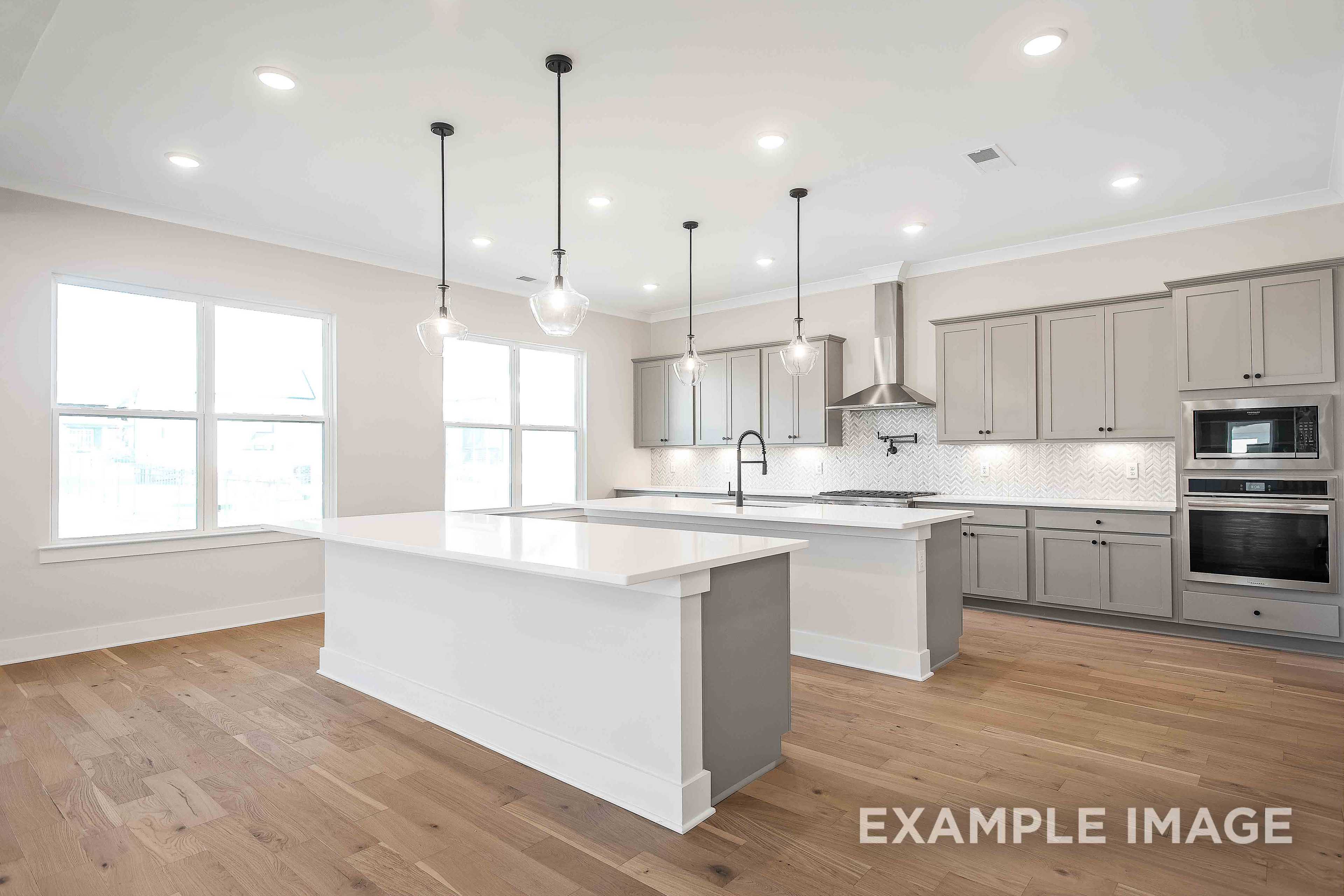 Spacious gourmet kitchen in The Alston A featuring large white quartz island, gray shaker cabinets, stainless appliances, and pendant lights