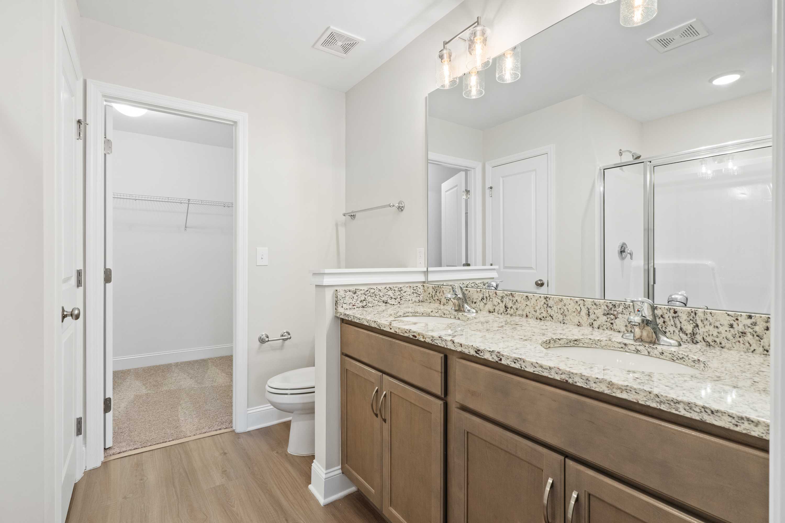 Spacious master bathroom in The Asheville featuring double granite vanity, frameless glass shower, and walk-in closet